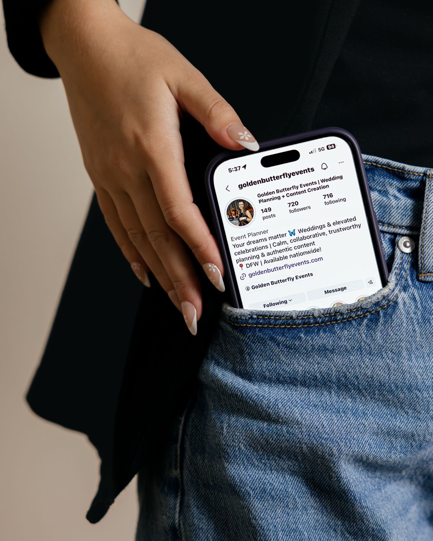 Hand holding a smartphone displaying an Instagram profile page tucked into blue jeans pocket.