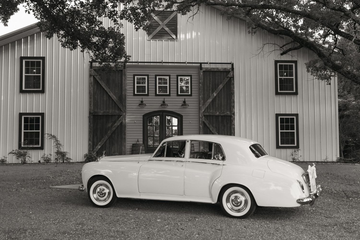 Vintage white Rolls-Royce parked in front of a classic barn venue in black and white photography.