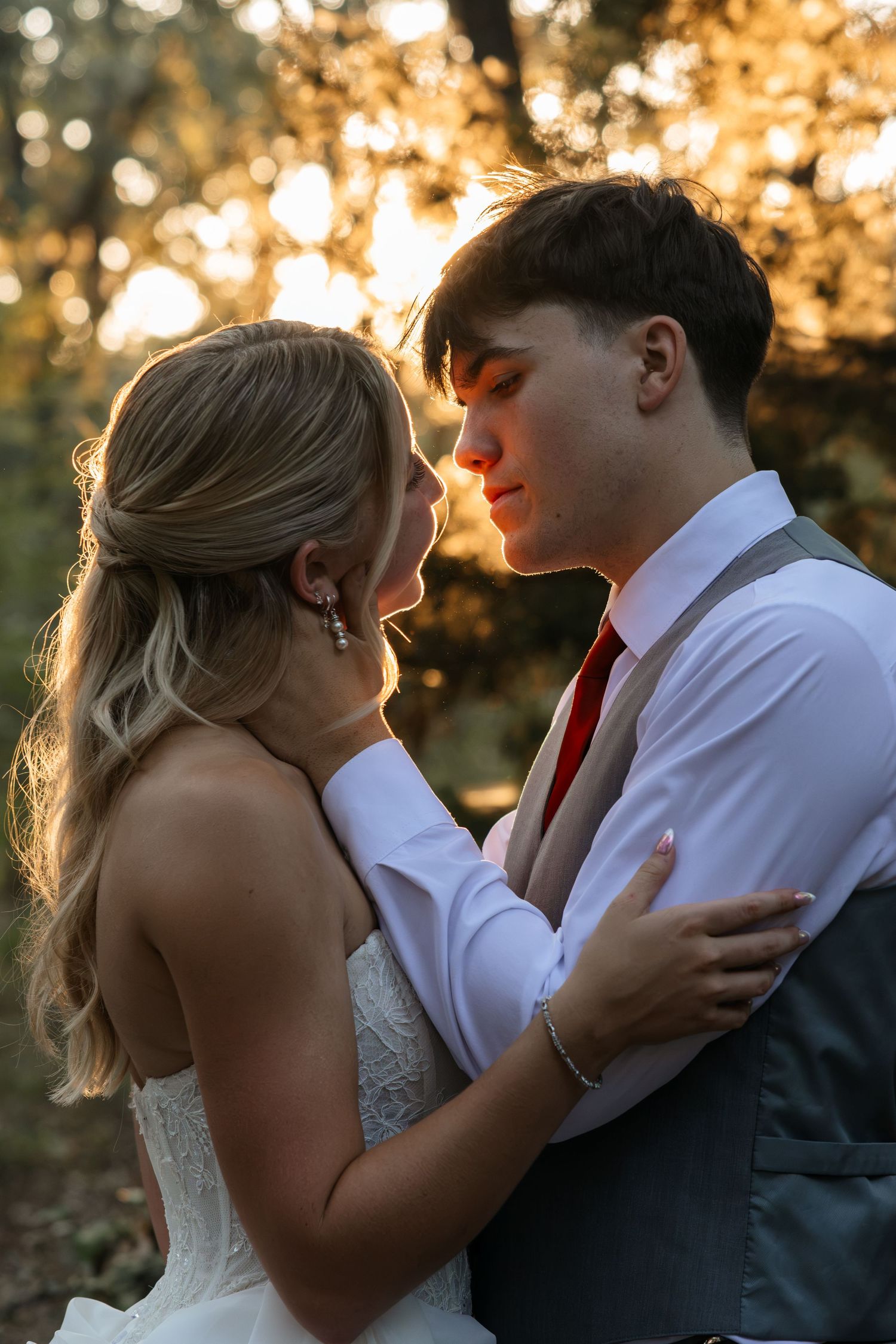 A bride and groom share a romantic moment outdoors at golden hour, embracing closely in wedding attire.