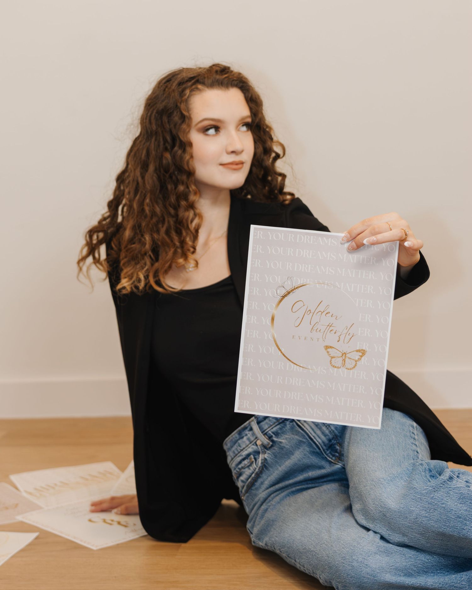 Young woman with curly hair sitting on floor holding a gold butterfly branded print poster.