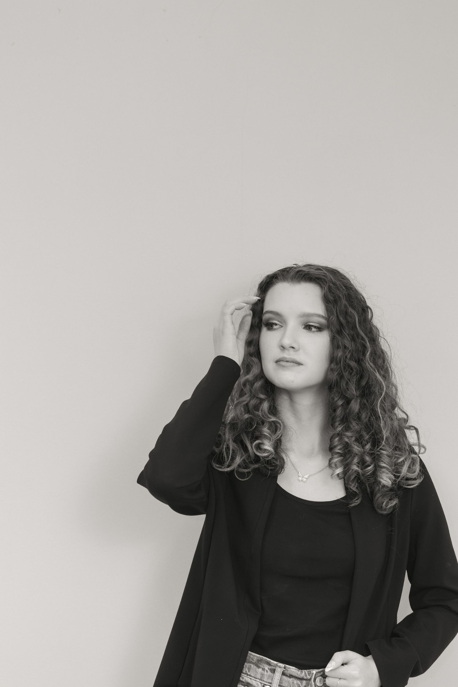 Black and white portrait of a young woman with curly hair wearing a black blazer, posing against a light background.
