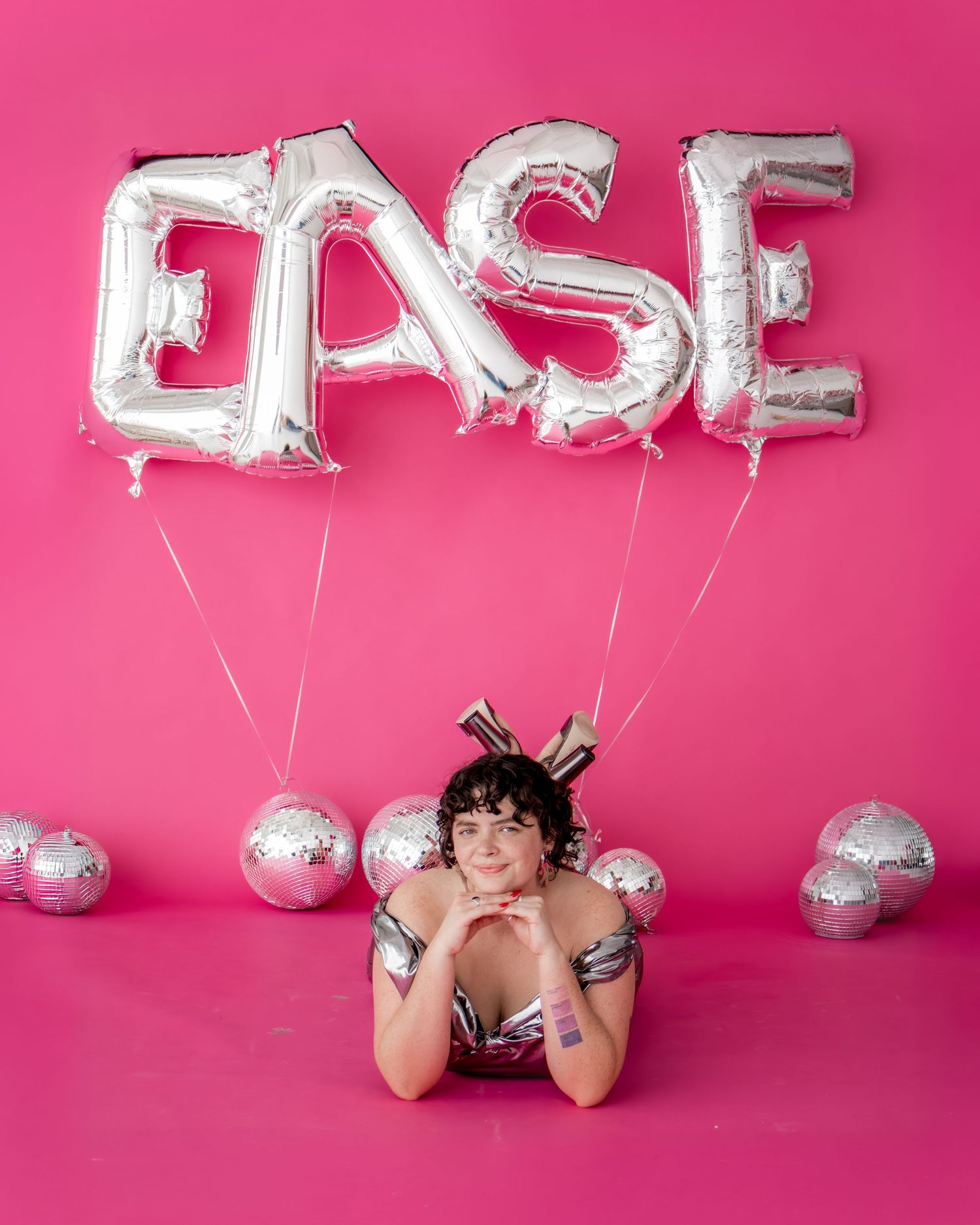 Person posing on pink backdrop with silver EASE letter balloons and disco ball decorations.