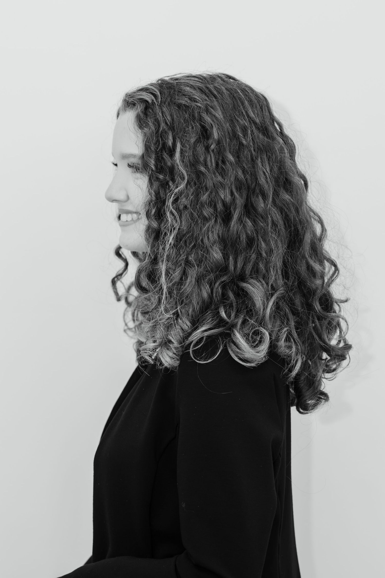 Black and white profile portrait of a young woman with long curly hair wearing a black top.