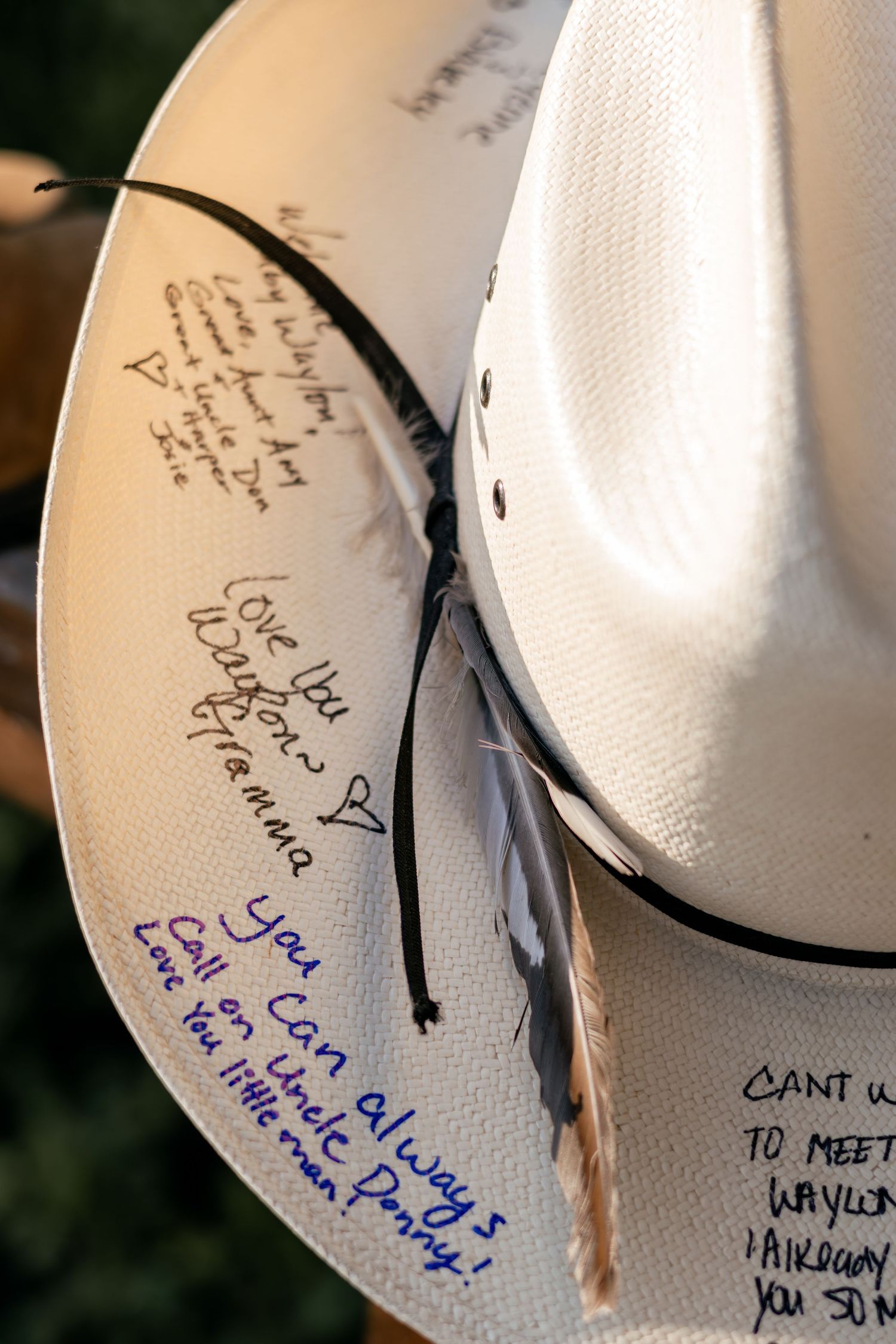 A white cowboy hat with handwritten messages and signatures in black and blue ink, featuring a black band and feather.