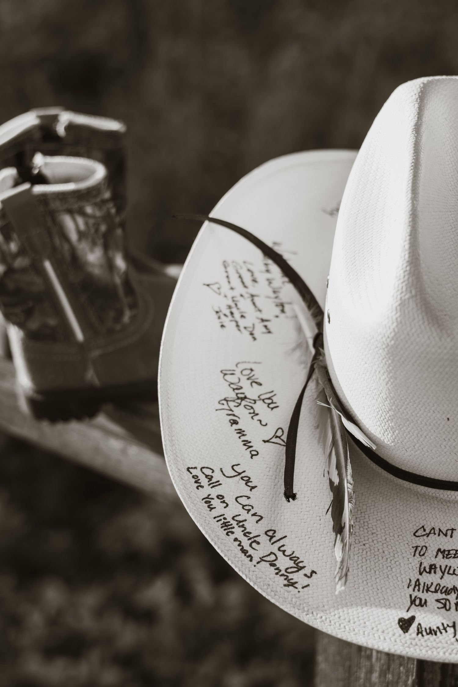 Black and white photo of a white cowboy hat with handwritten signatures resting on a wooden fence.