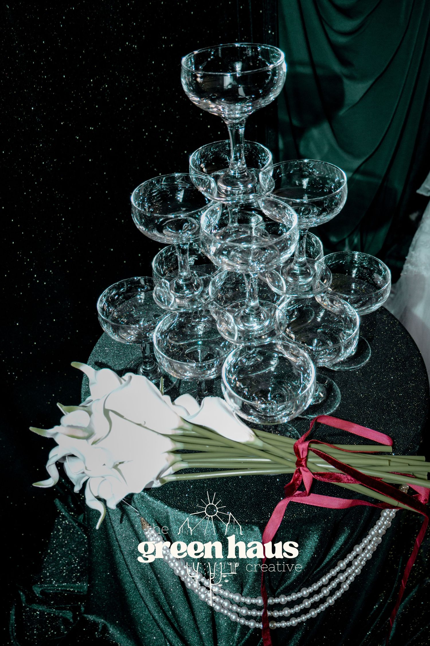Crystal champagne coupes arranged in rows with white lilies and green stems against a dark background.