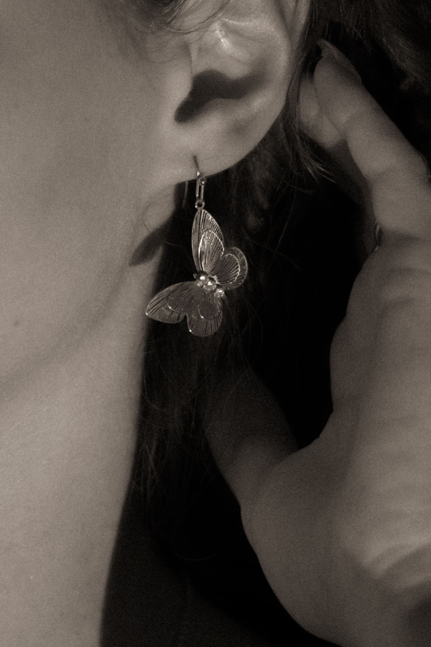 Close-up black and white photo of a woman wearing a delicate silver butterfly drop earring.