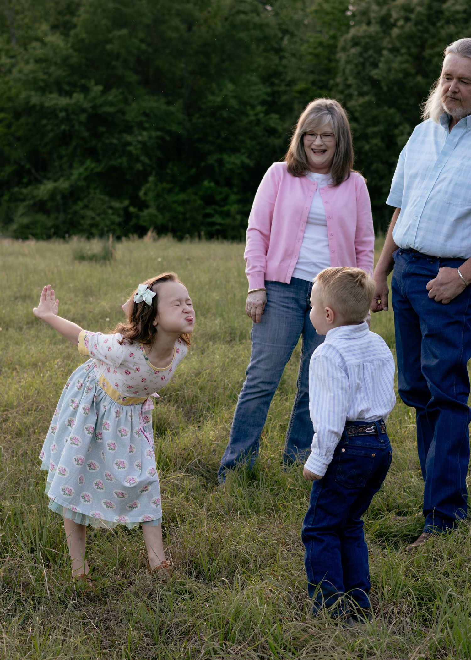 Two children play in a grassy field while grandparents watch and smile during an outdoor family photo session.