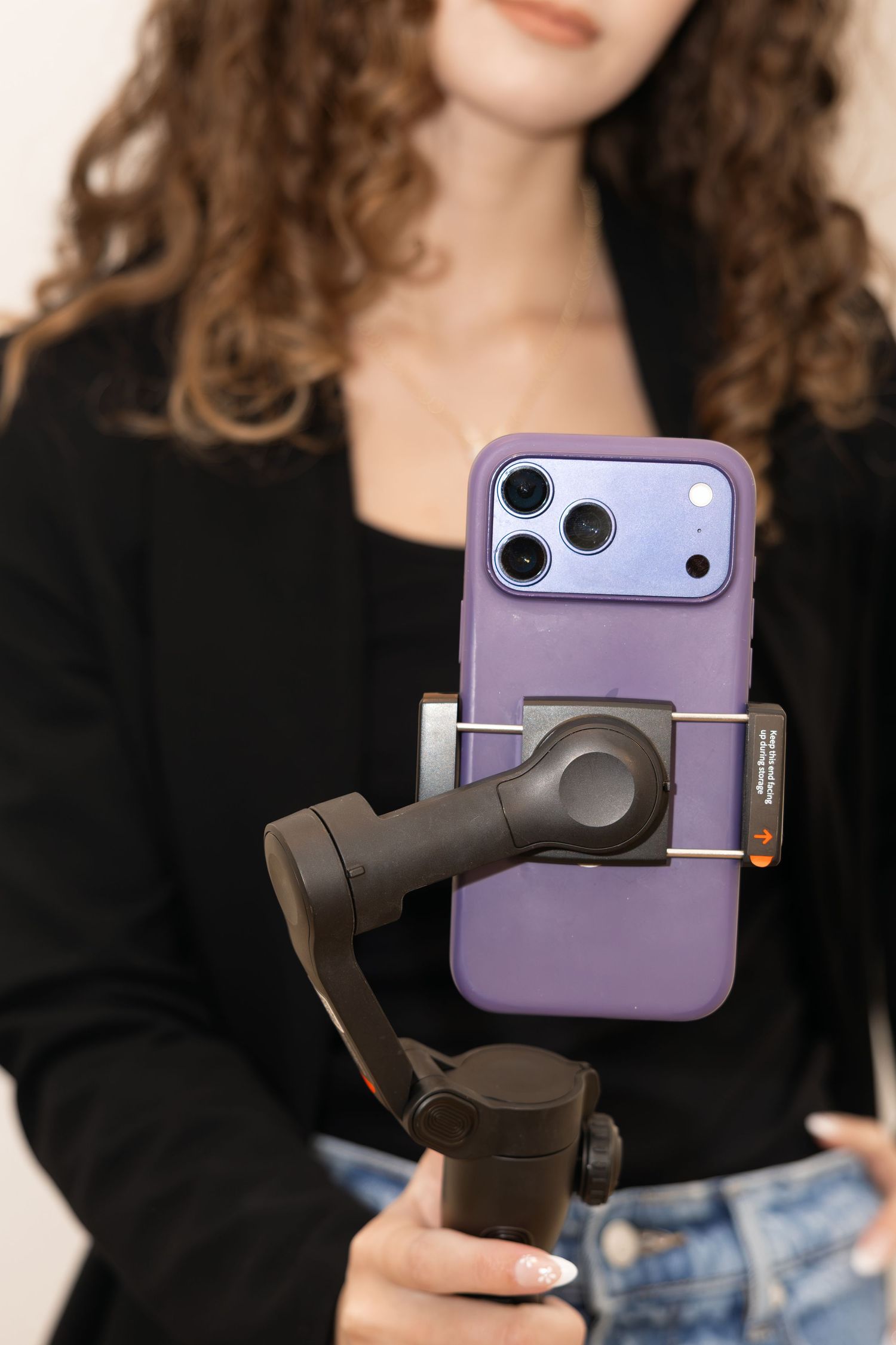 Woman in black blazer holding smartphone on gimbal stabilizer with purple iPhone case for content creation.