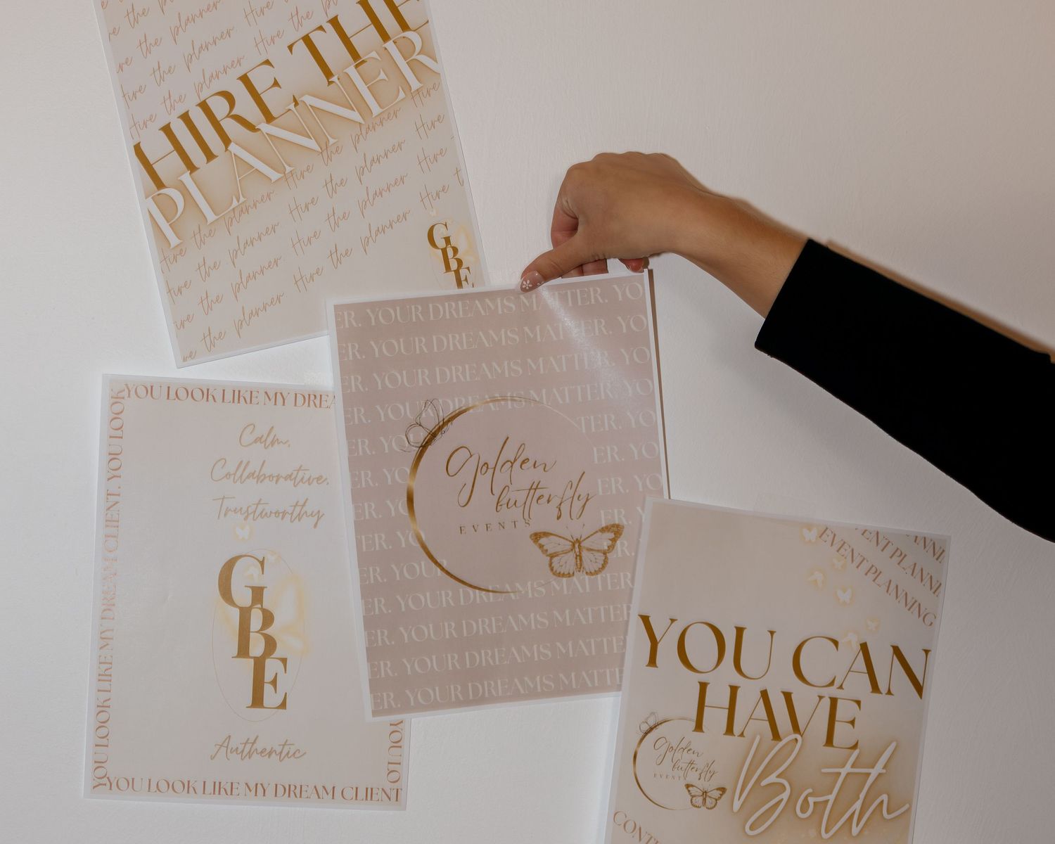 Hand holding gold and white motivational print designs including 