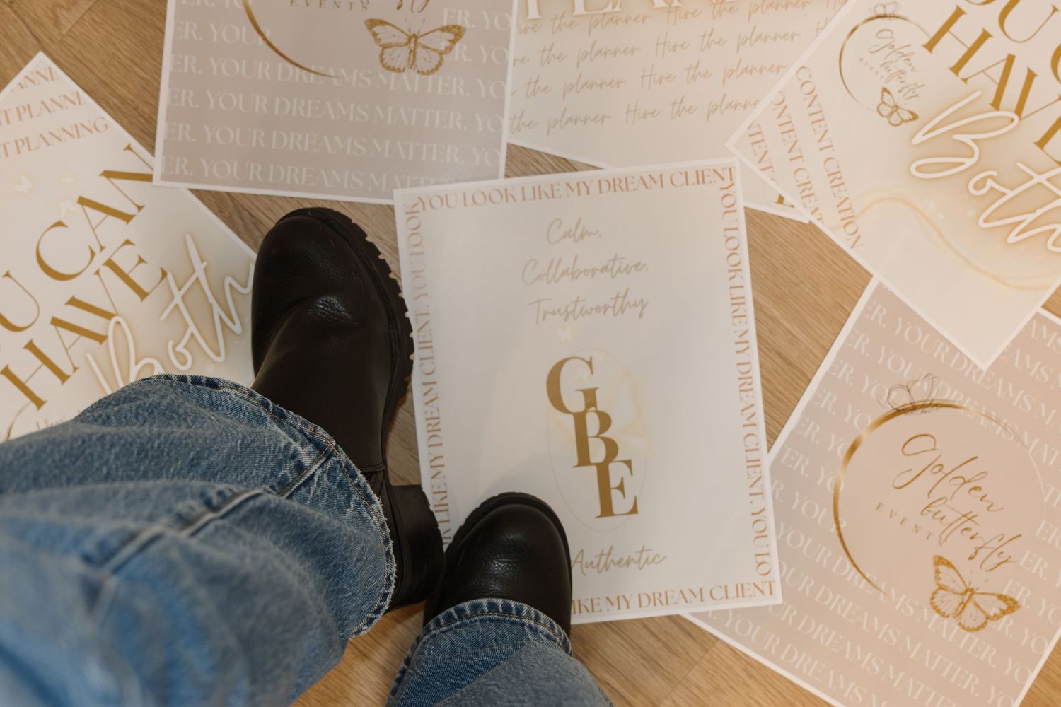 Person standing over gold foil motivational cards and GBE branding materials on a light wooden floor.