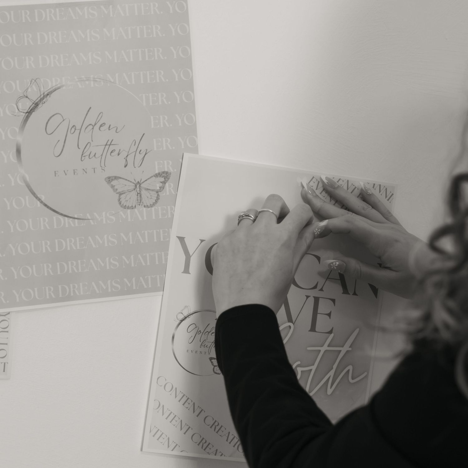 Black and white photo of hands applying vinyl decals featuring Golden Butterfly Events branding and motivational text.