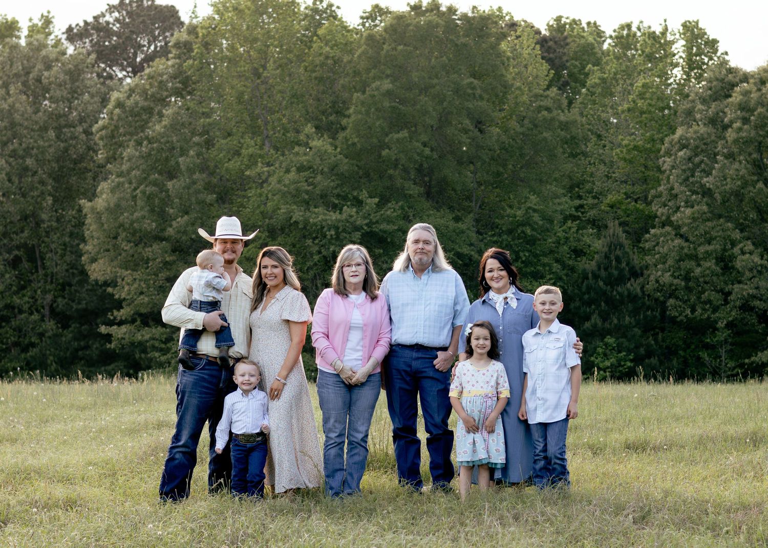 Large family portrait in a green field with parents, grandparents, and children dressed in country style attire.