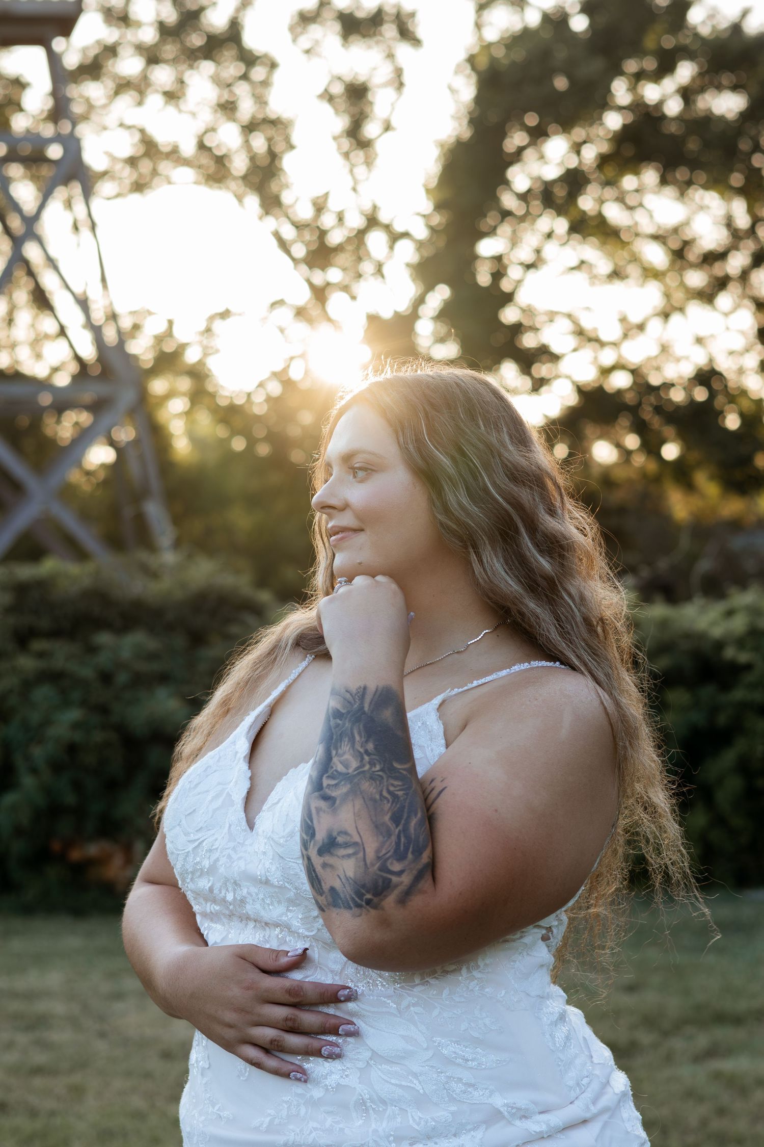 Bride in white lace gown with lion tattoo on arm, posing outdoors at golden hour sunset.