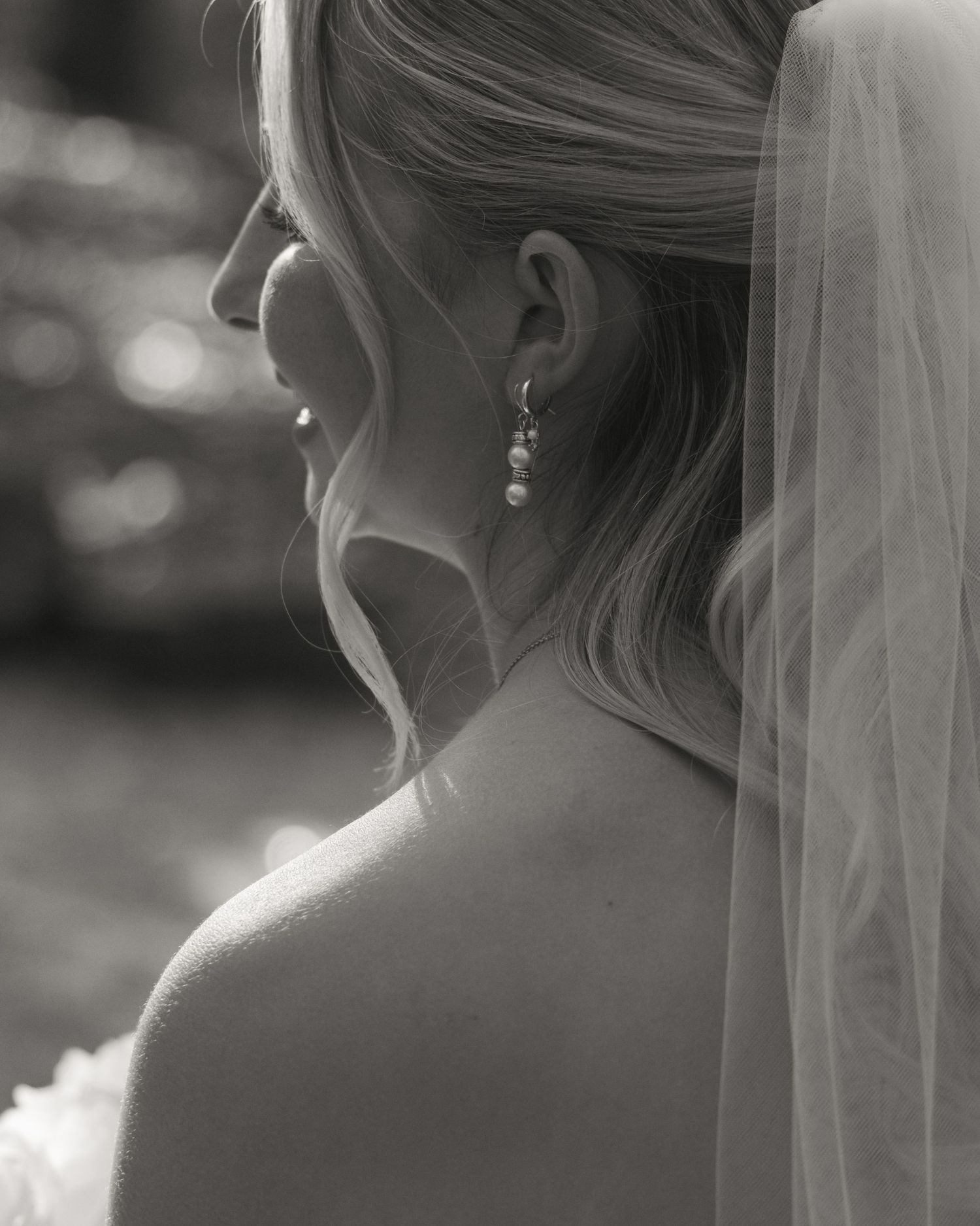 Black and white close-up of bride wearing pearl drop earring and elegant veil on wedding day.