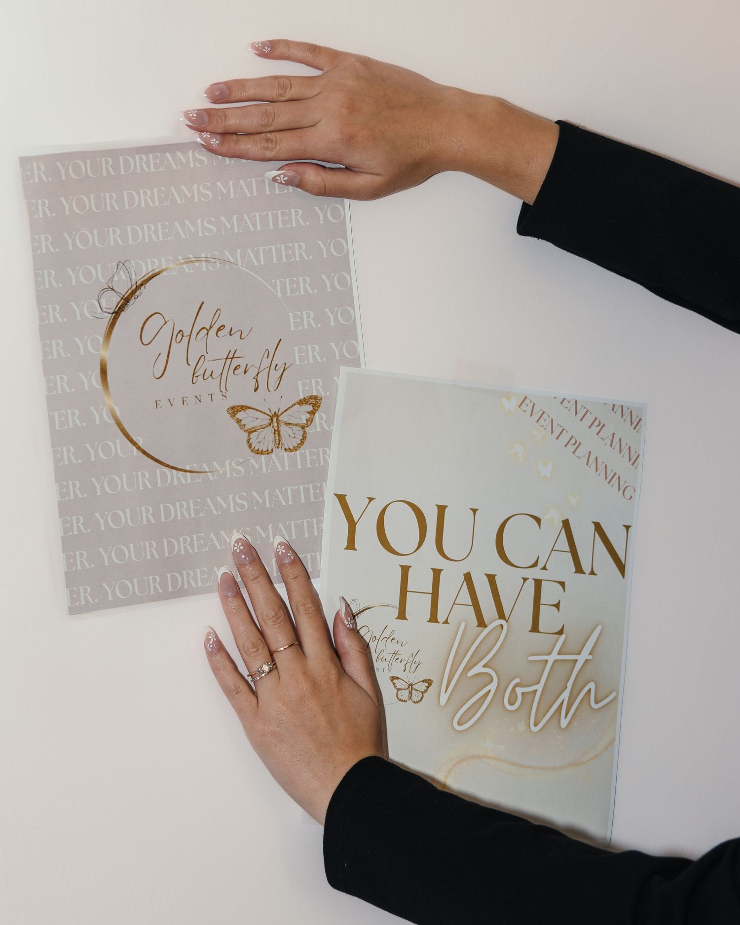 Hands holding two elegant gold and beige event planning brochures with butterfly logo and motivational text.