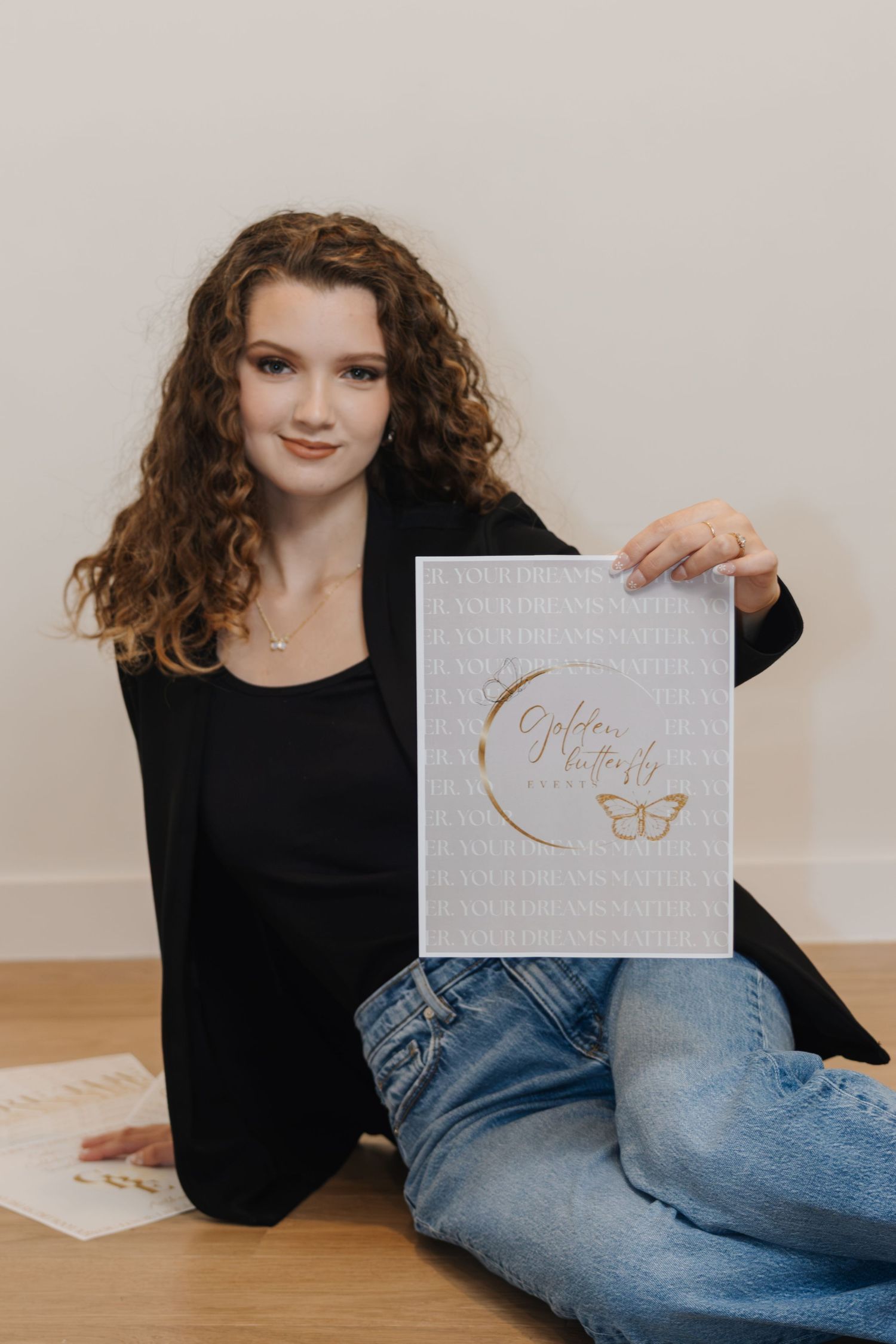 Young woman with curly hair sitting on floor holding a gray and gold butterfly print poster.