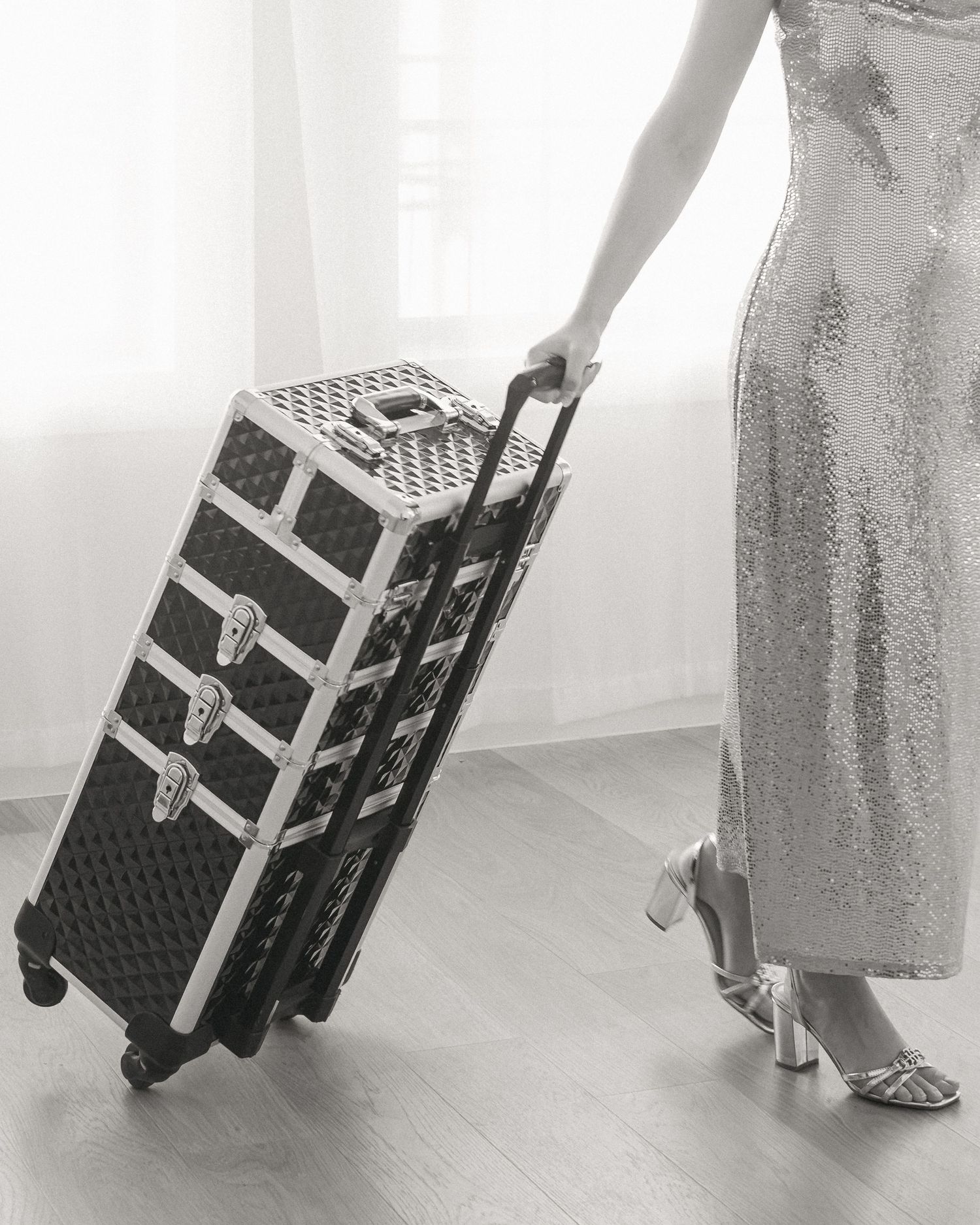 Woman in silver sequin gown pulling a rolling makeup artist trunk case, black and white photo.