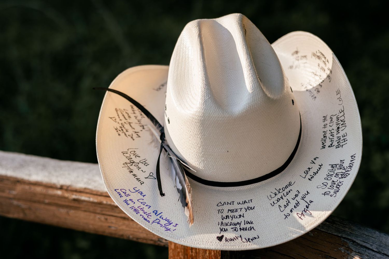 White cowboy hat covered in handwritten signatures and messages resting on a wooden railing outdoors.
