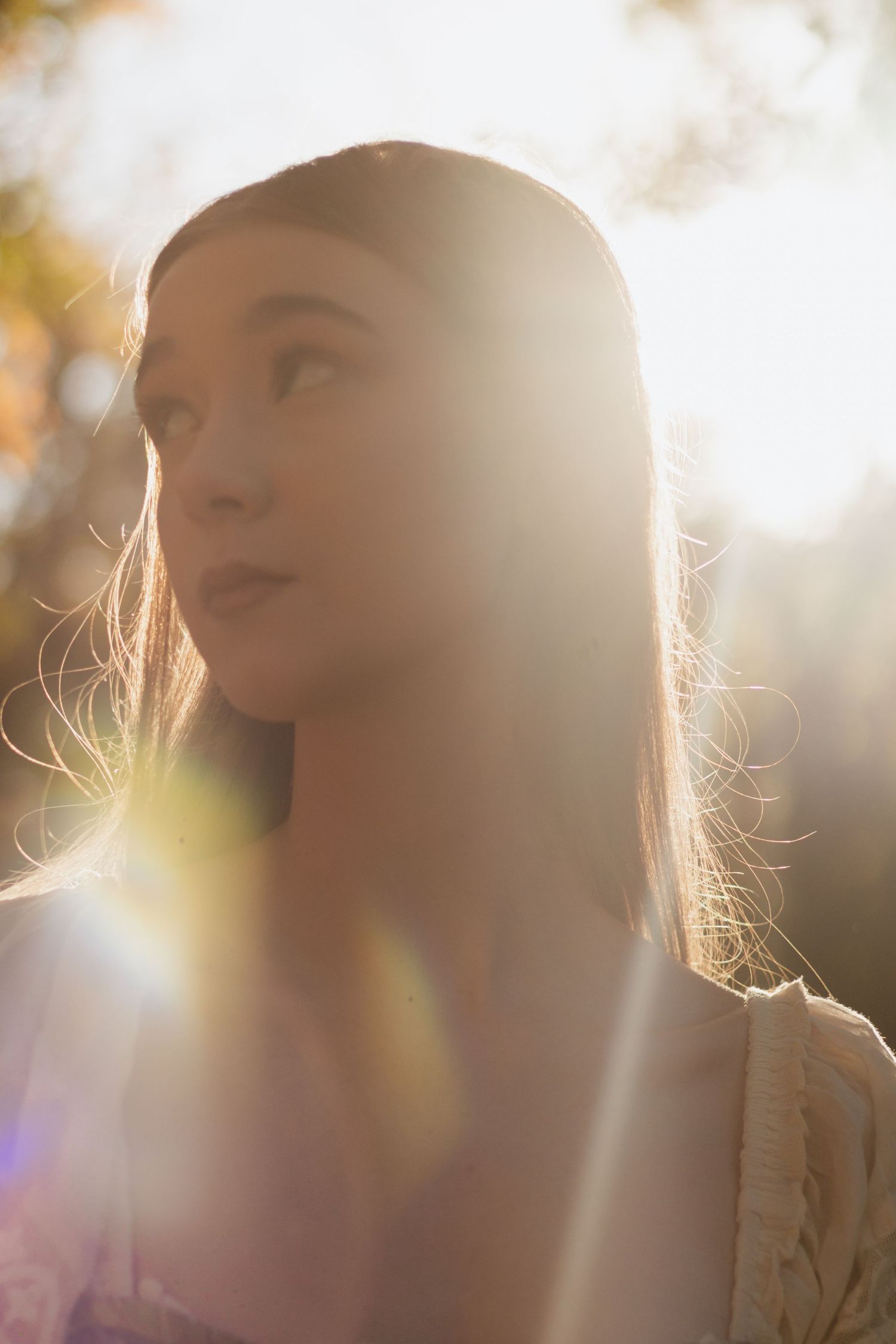 Ethereal sunlit portrait with dreamy lens flares creating a magical golden hour atmosphere.
