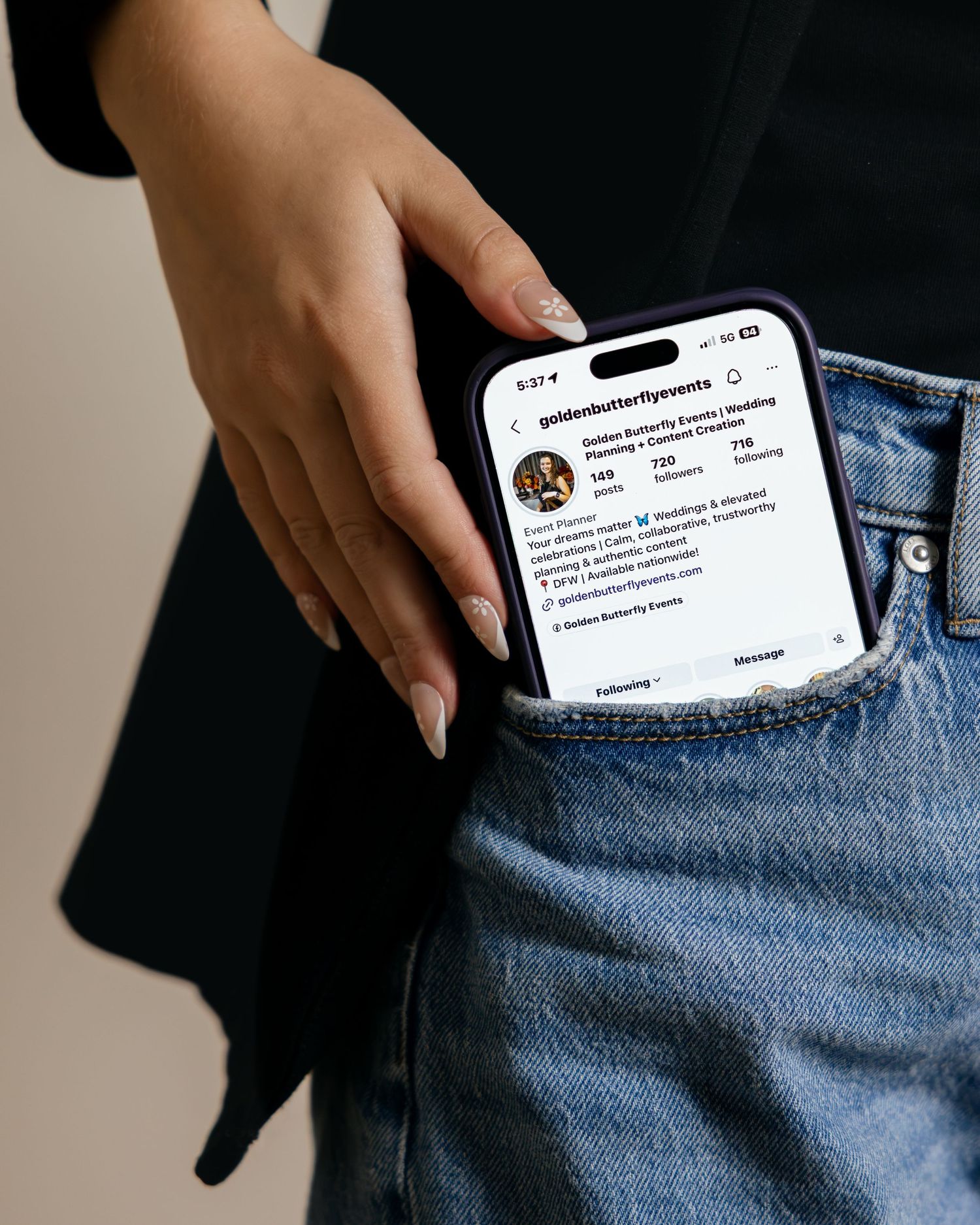 Hand placing iPhone showing Golden Butterfly Events Instagram profile into jeans pocket.
