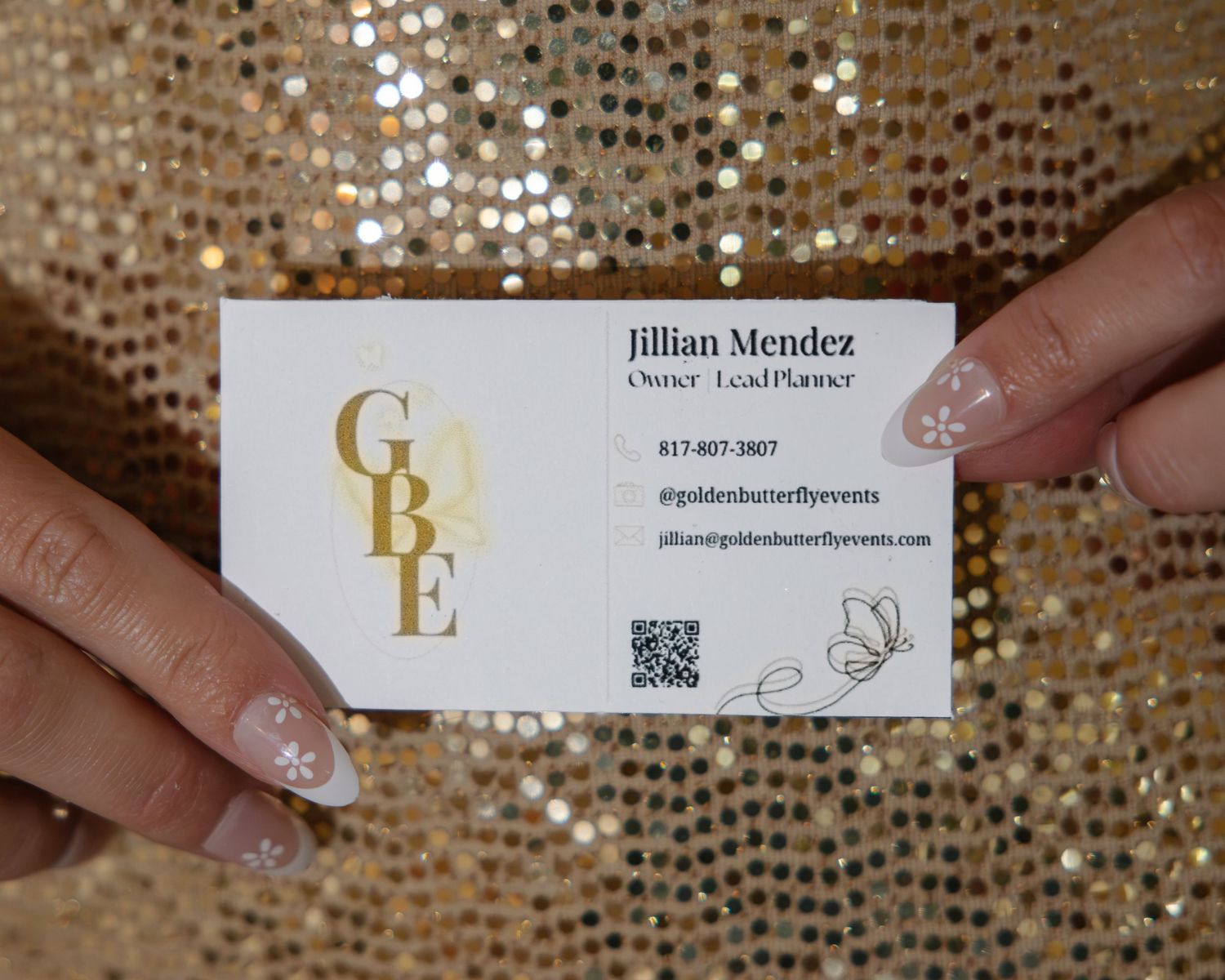 Jillian Mendez Golden Butterfly Events business card held against a gold sequin background.