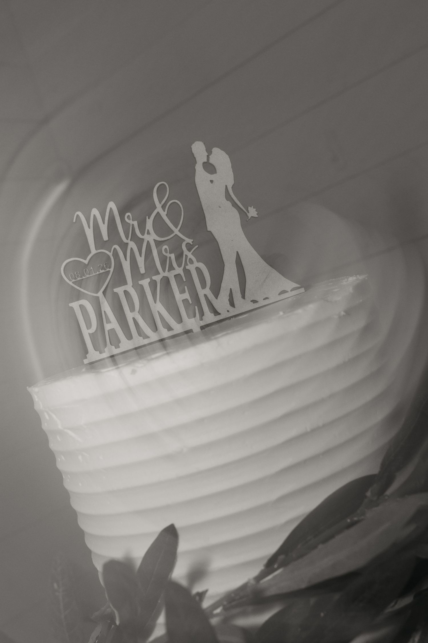 Black and white photo of elegant white tiered wedding cake with Mr. and Mrs. Parker cake topper.