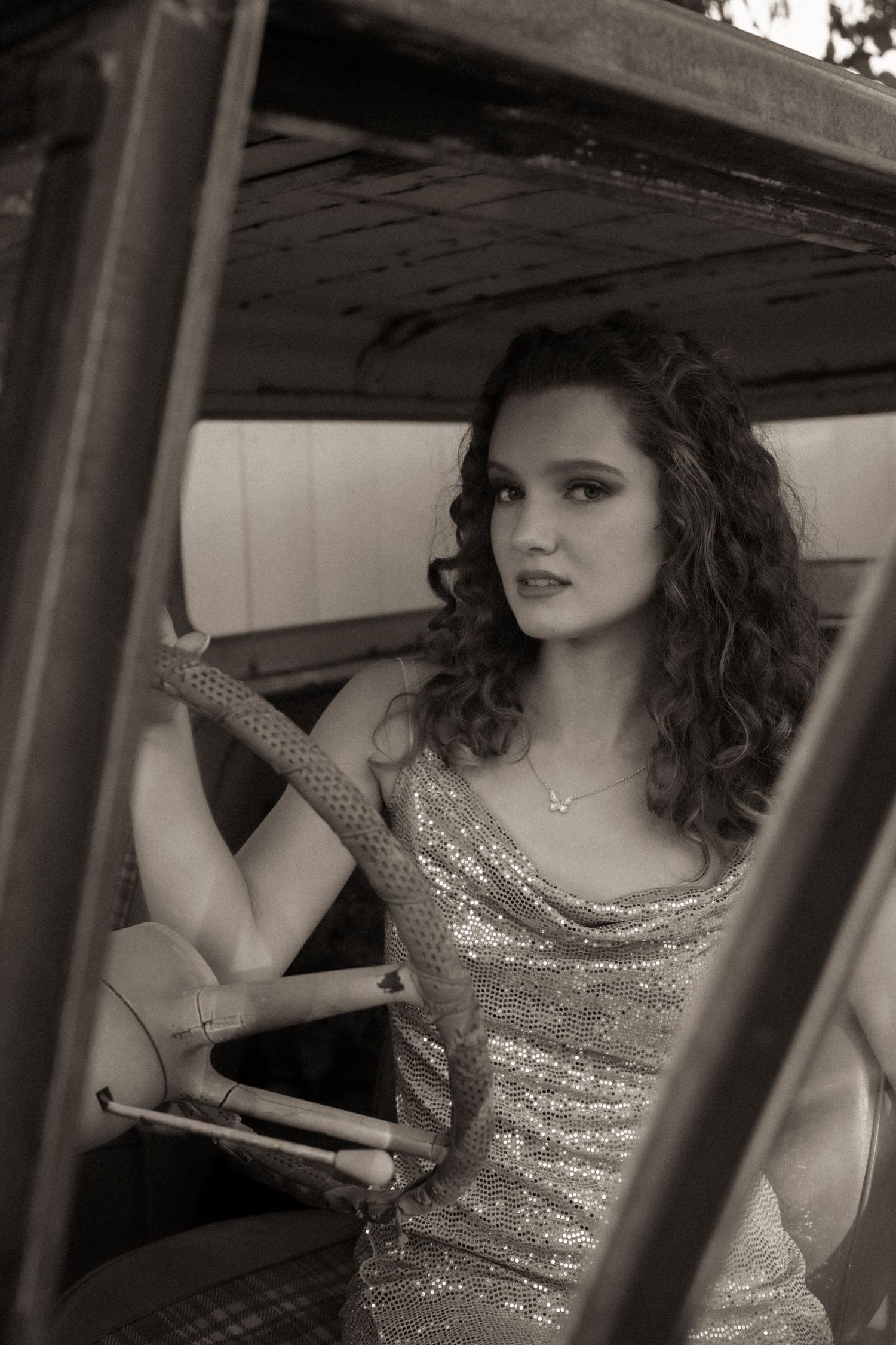 Young woman in a sequin dress sitting behind the wheel of a vintage truck, sepia tone photo.