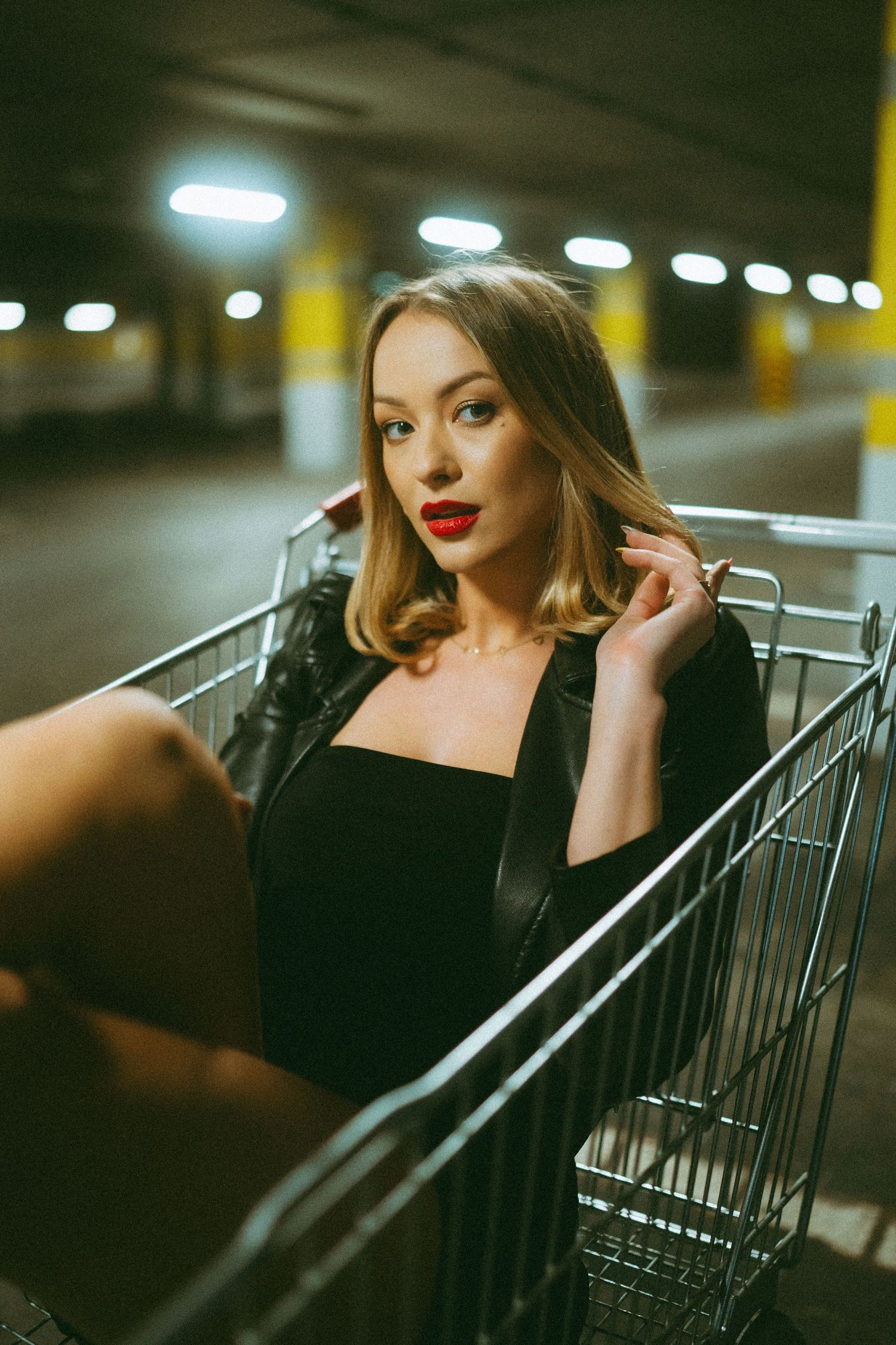 Glamorous portrait of a woman in black attire sitting in a shopping cart.