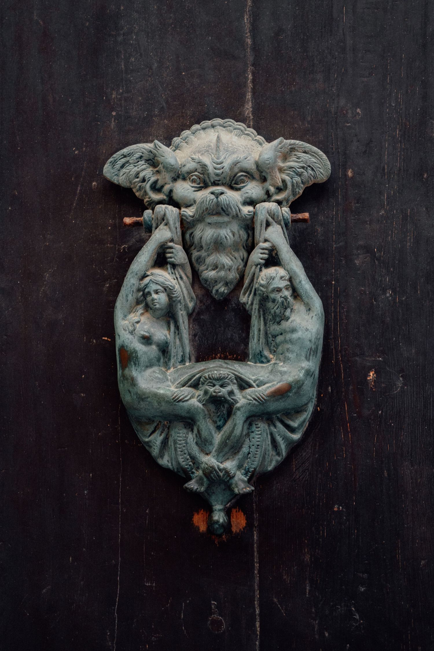 Ornate bronze door knocker featuring classical figures on a dark wooden door.
