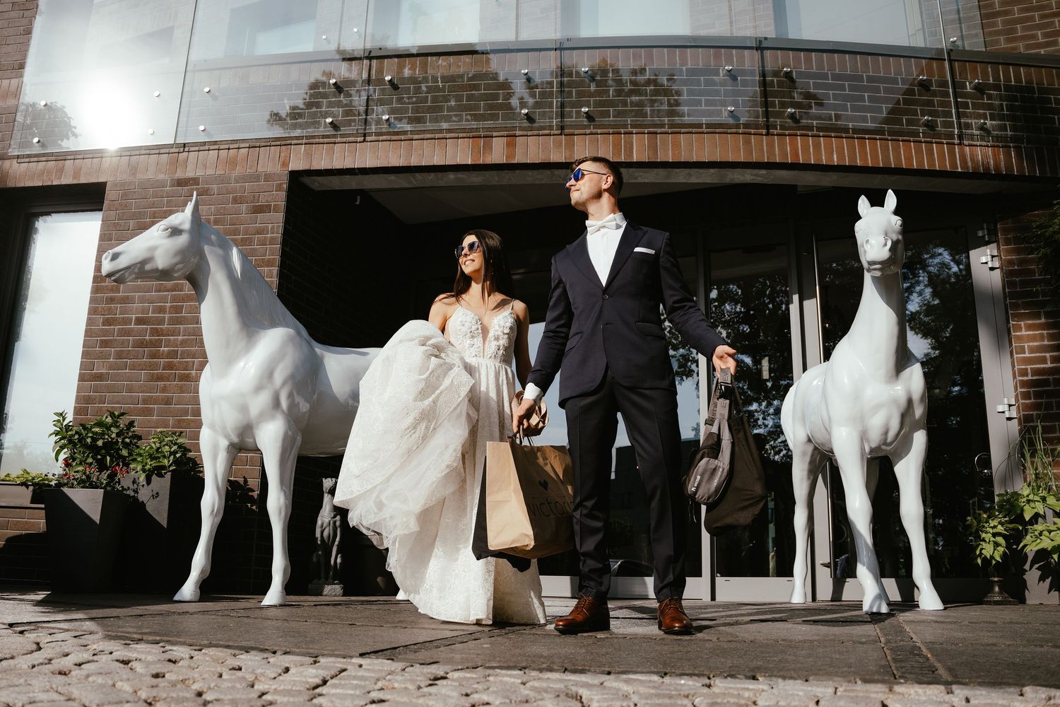Wedding couple walking with white dog outside brick building.
