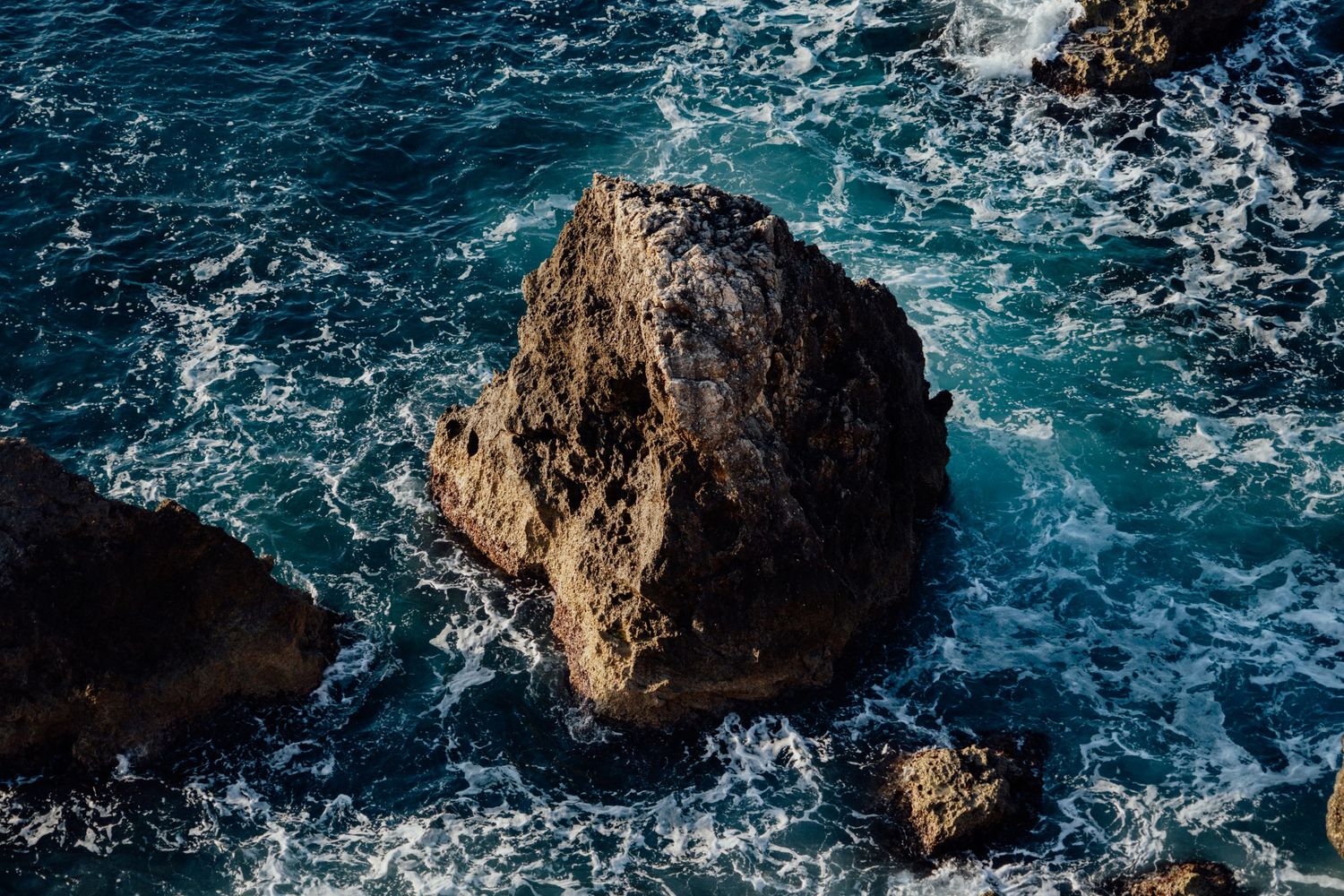 Dramatic waves crashing against rocky coastal cliffs with turquoise blue ocean waters.