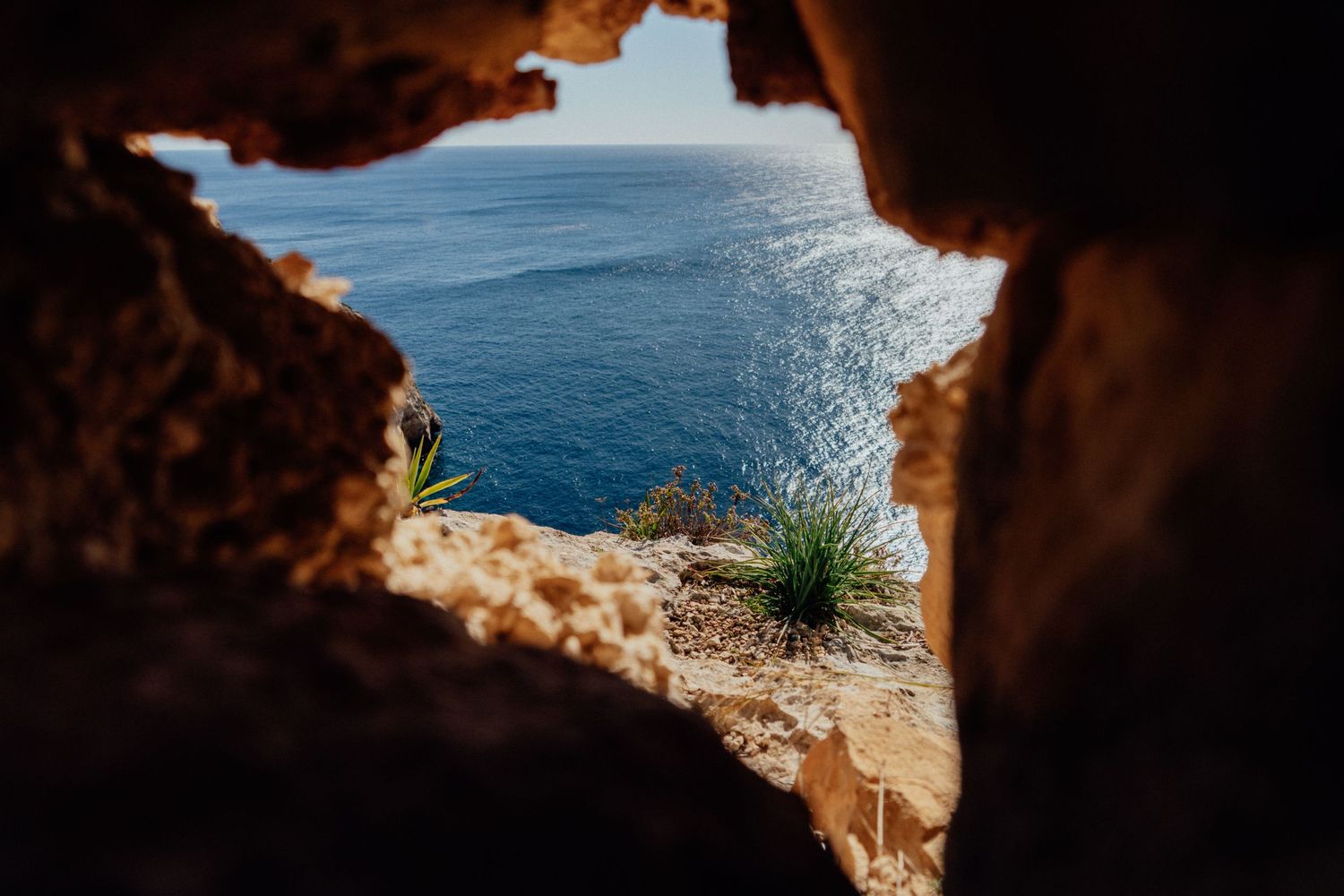 Natural cave opening frames a stunning view of blue ocean waters and rocky coastline.