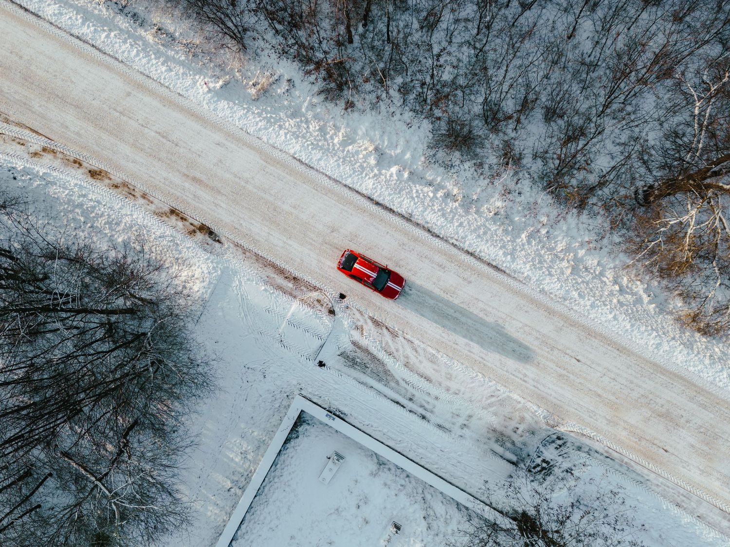 Aerial view of a red car driving on a snow-covered road through a winter forest.