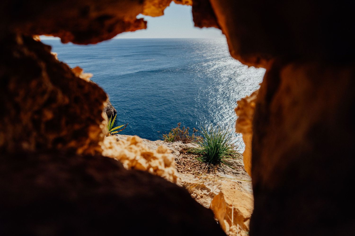 Ocean view framed through a natural rock arch formation at sunset.