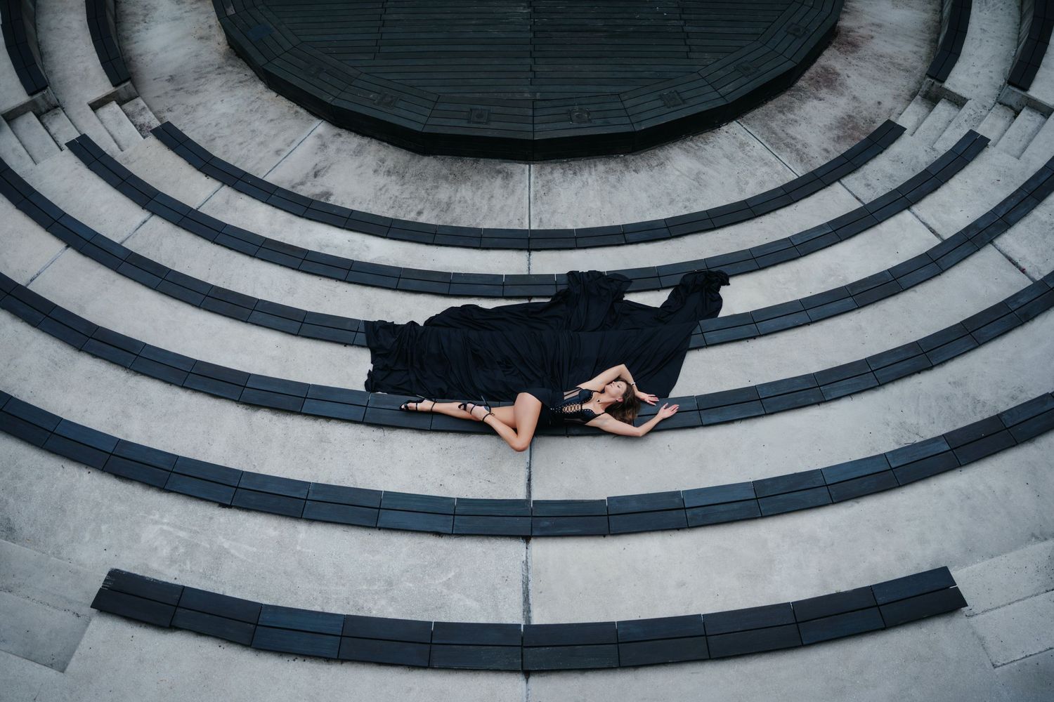 Aerial view of a person in black clothing lying on curved concrete steps in a circular architectural pattern.