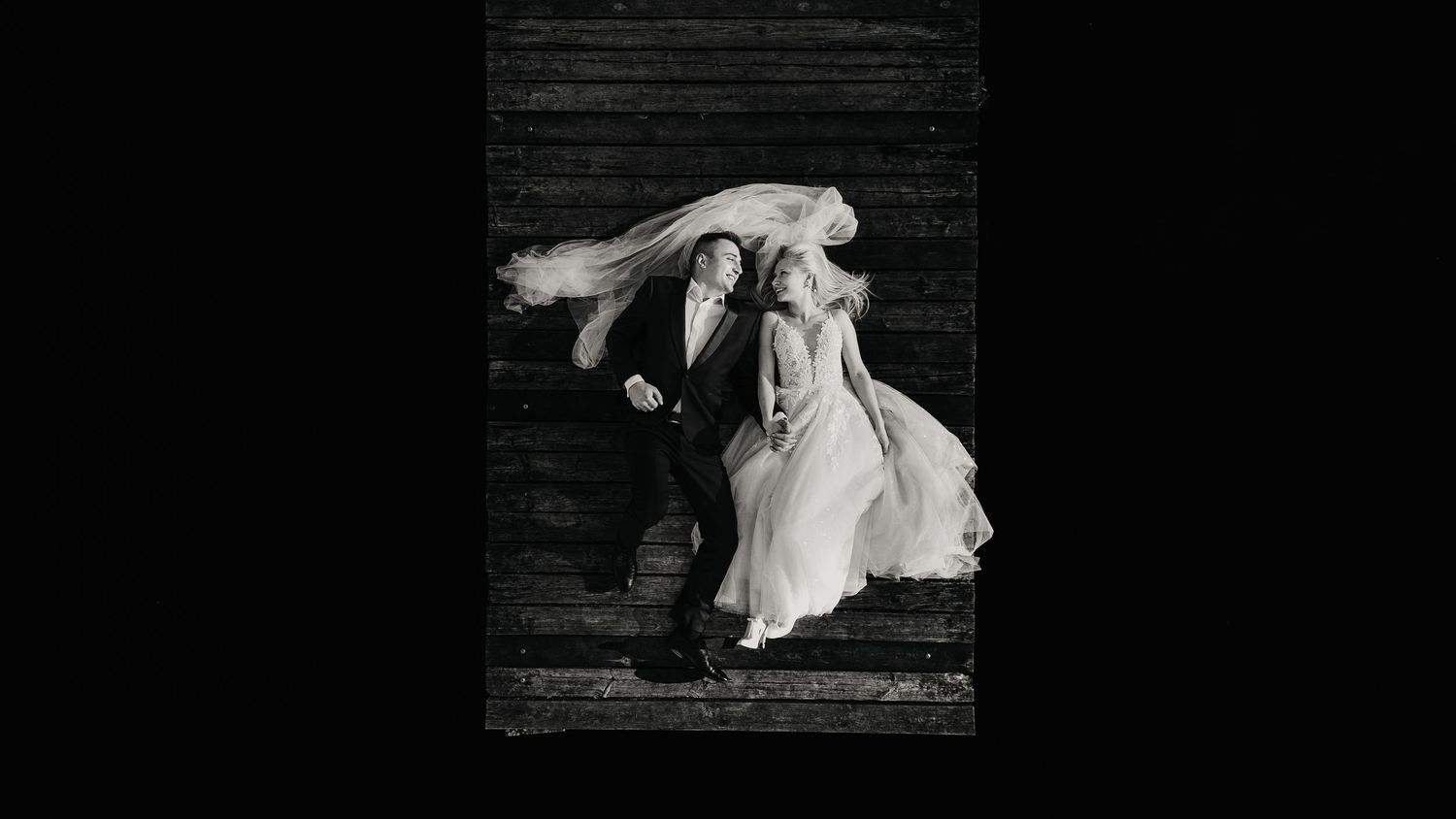 Dramatic black and white photo of a flowing wedding dress in motion on wooden stairs.