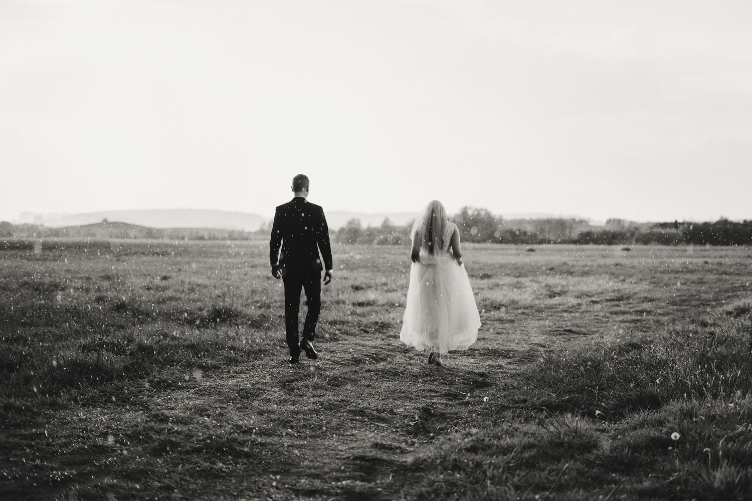 A couple walks together through a scenic meadow at dusk in black and white photography.