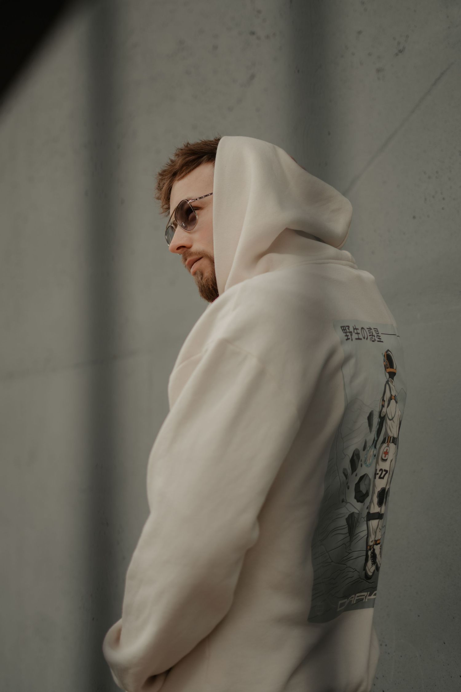 Side profile view of someone wearing a white hoodie with graphic print against a concrete wall.