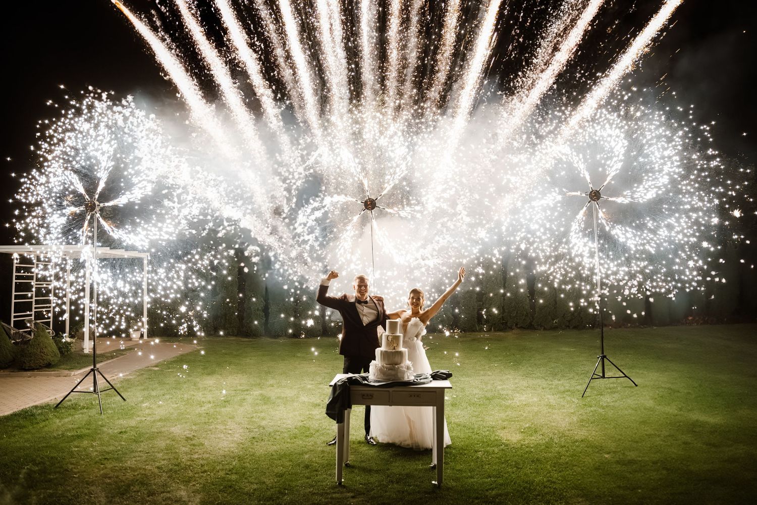 Spectacular fireworks display illuminates a nighttime wedding celebration on a grassy lawn.