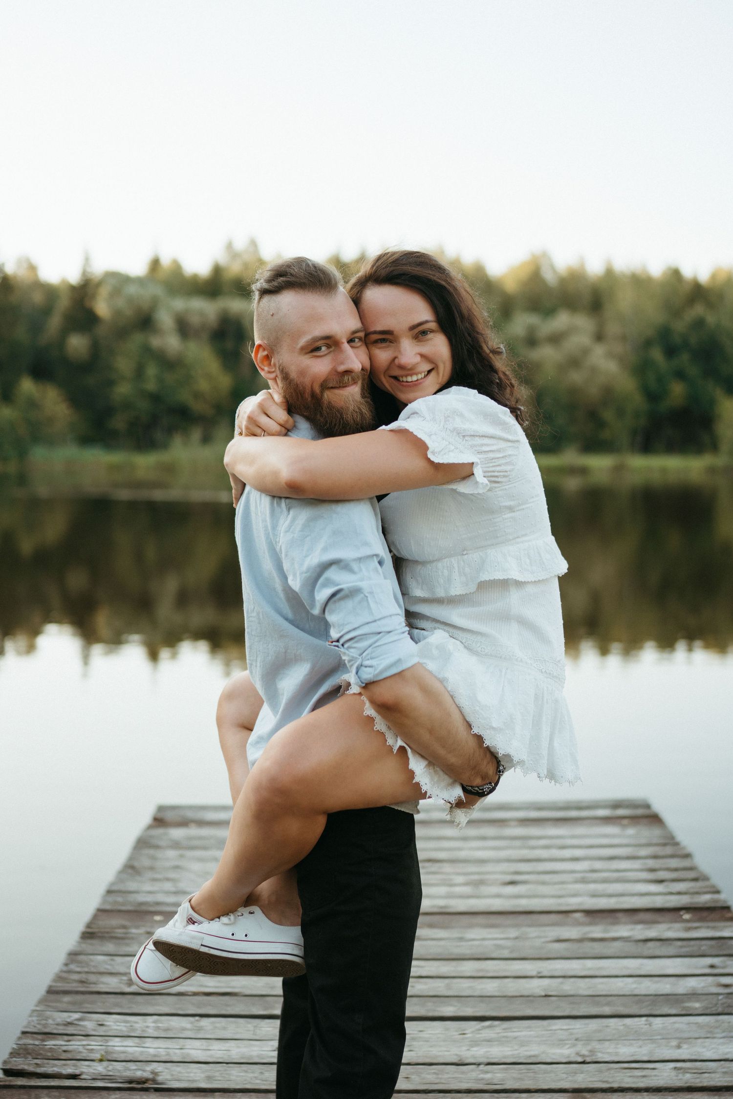 Romantic couple embracing on wooden dock by lake at sunset.