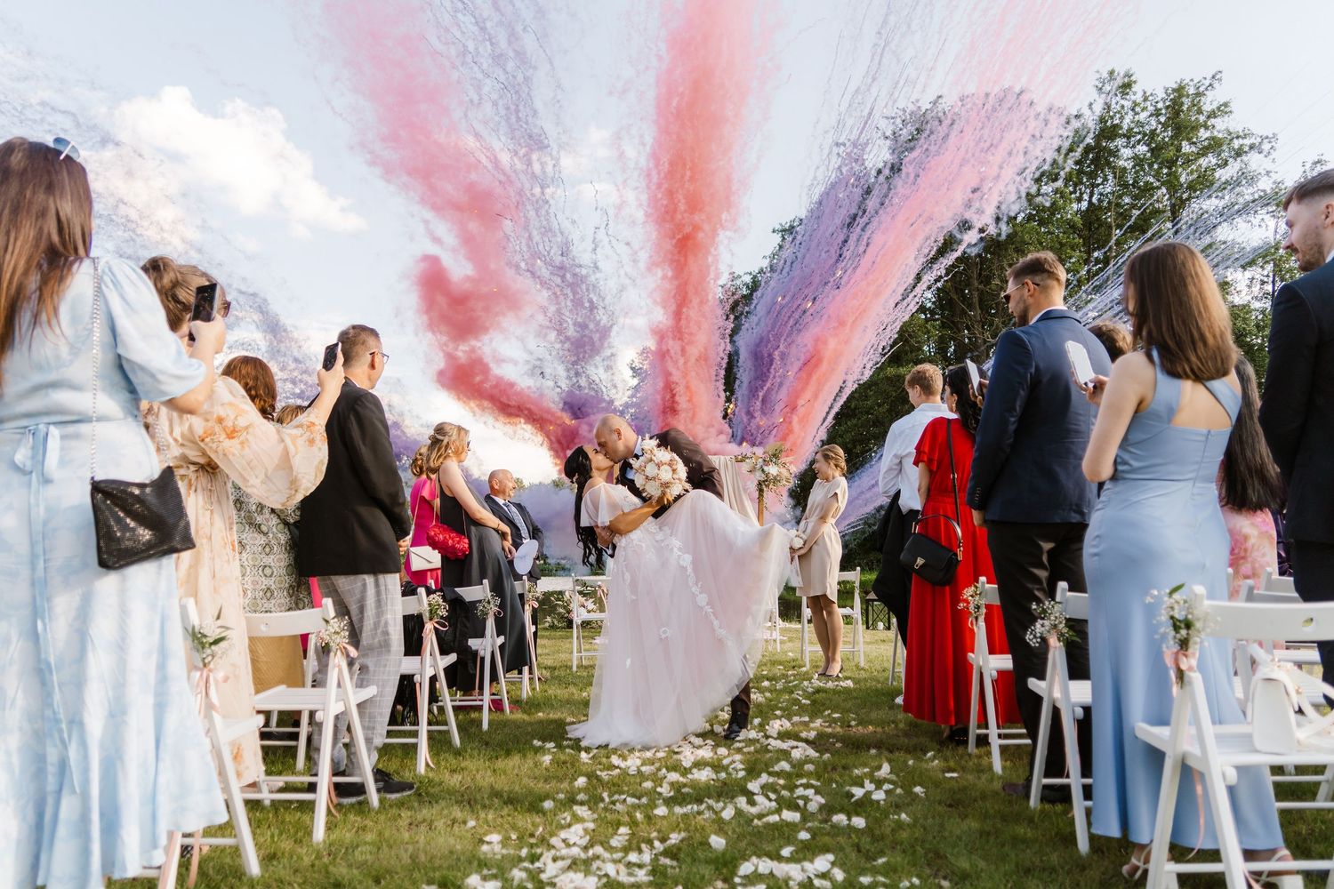 Wedding ceremony exit with colorful smoke bombs creating pink and red effects in the air.