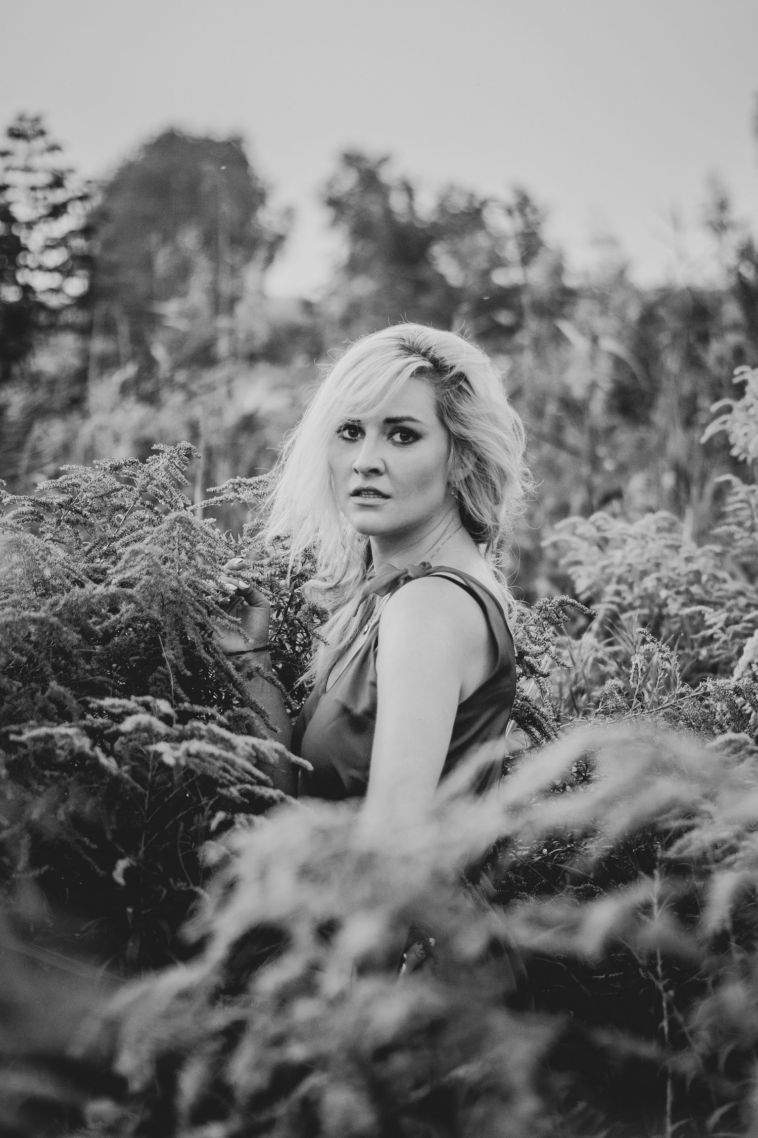 A black and white portrait series of a woman lying among ferns and foliage in an outdoor setting.