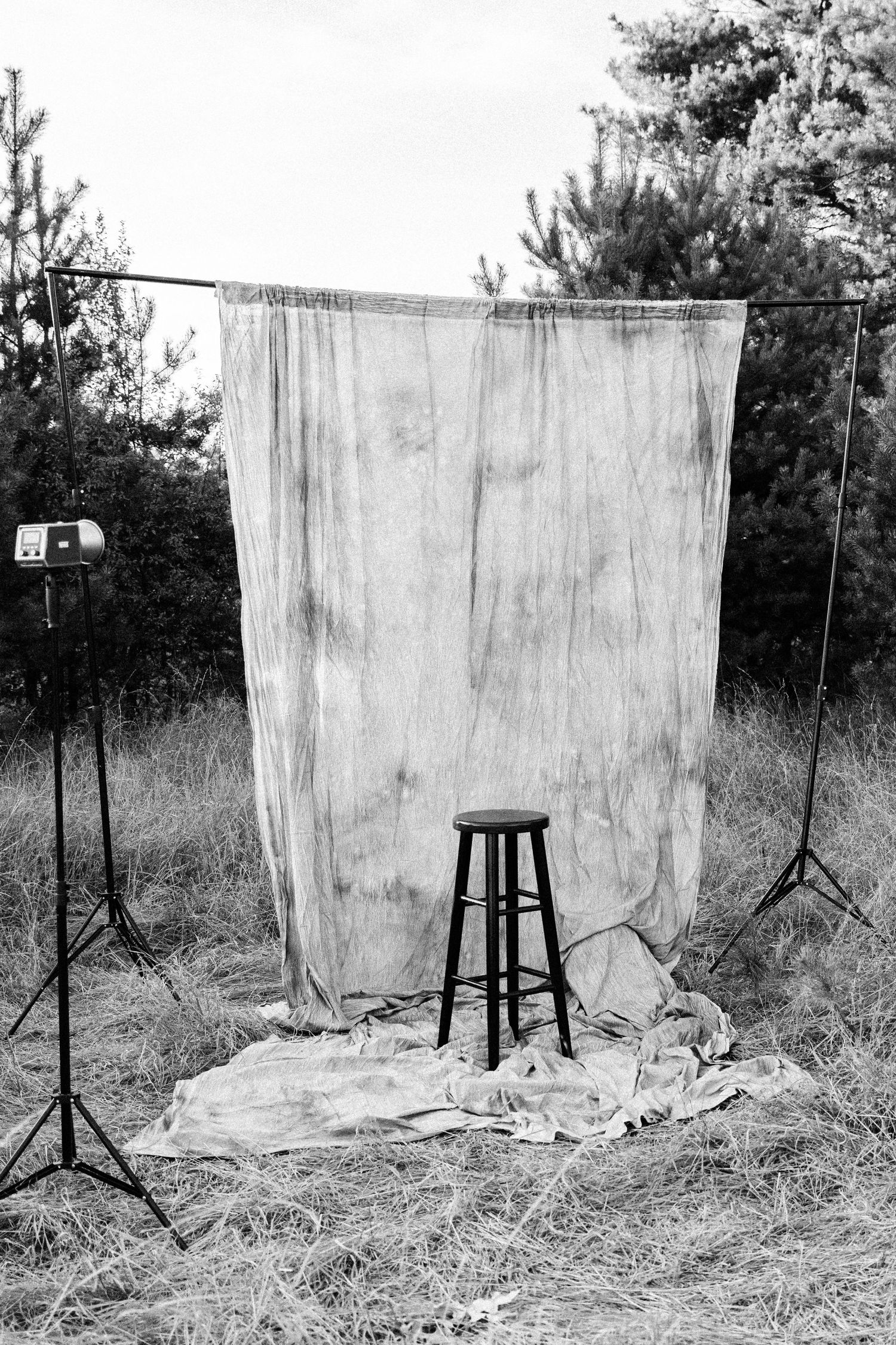 Black and white outdoor photo studio setup with backdrop, stool, and studio light on stands in a field.