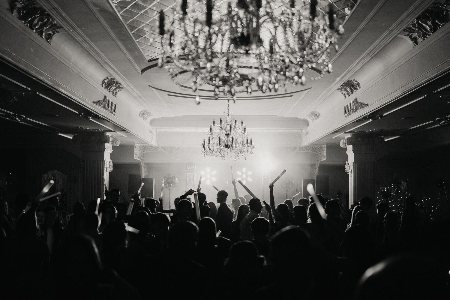 Black and white photo of a crowded dance floor under elegant crystal chandeliers.