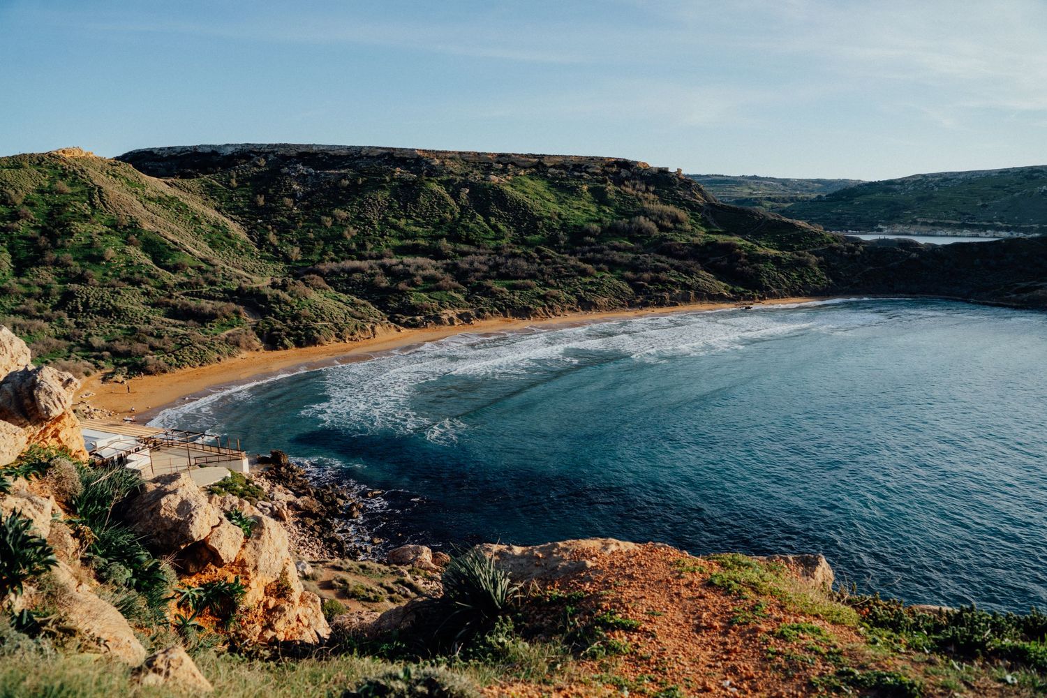 Panoramic vista of a curved bay with dramatic cliffs and coastal vegetation.