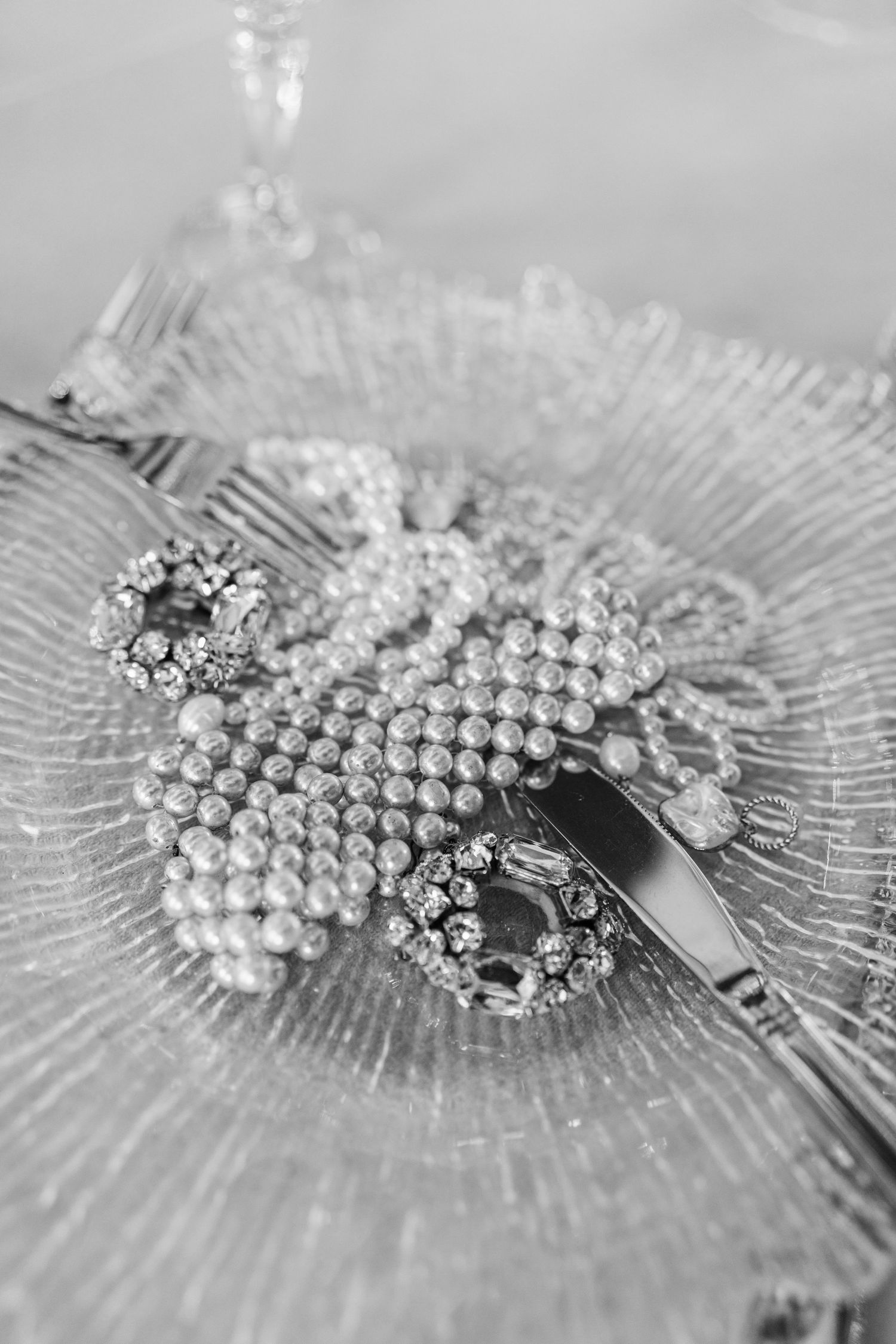 Elegant pearl necklace and crystal brooches arranged on a textured glass plate in black and white.