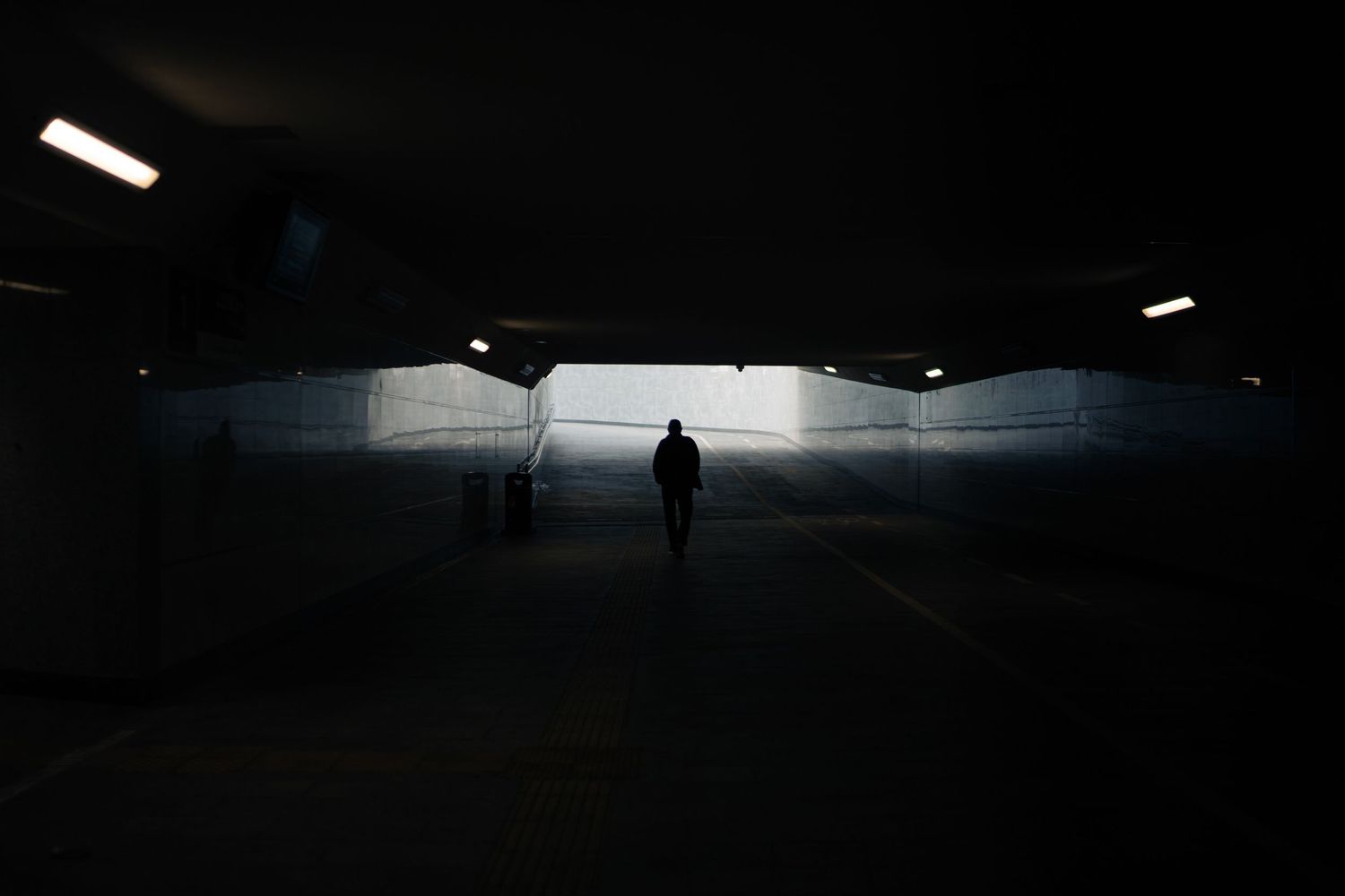 Silhouette of person walking in dark underground tunnel with distant light.