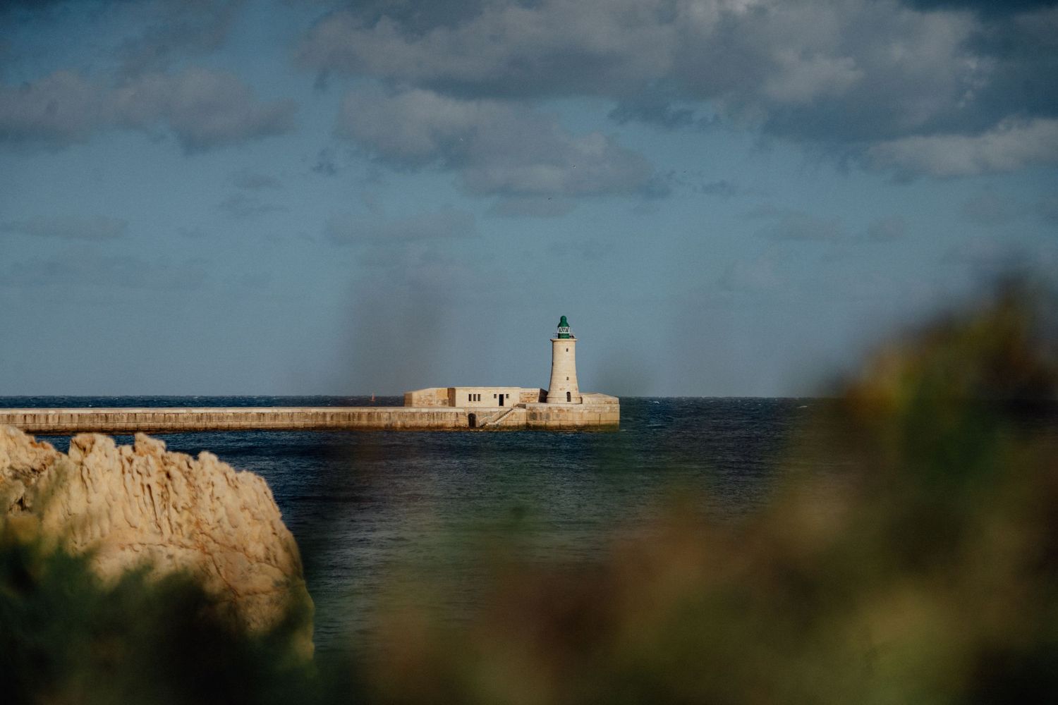 Coastal lighthouse viewed through natural foliage against blue ocean backdrop.