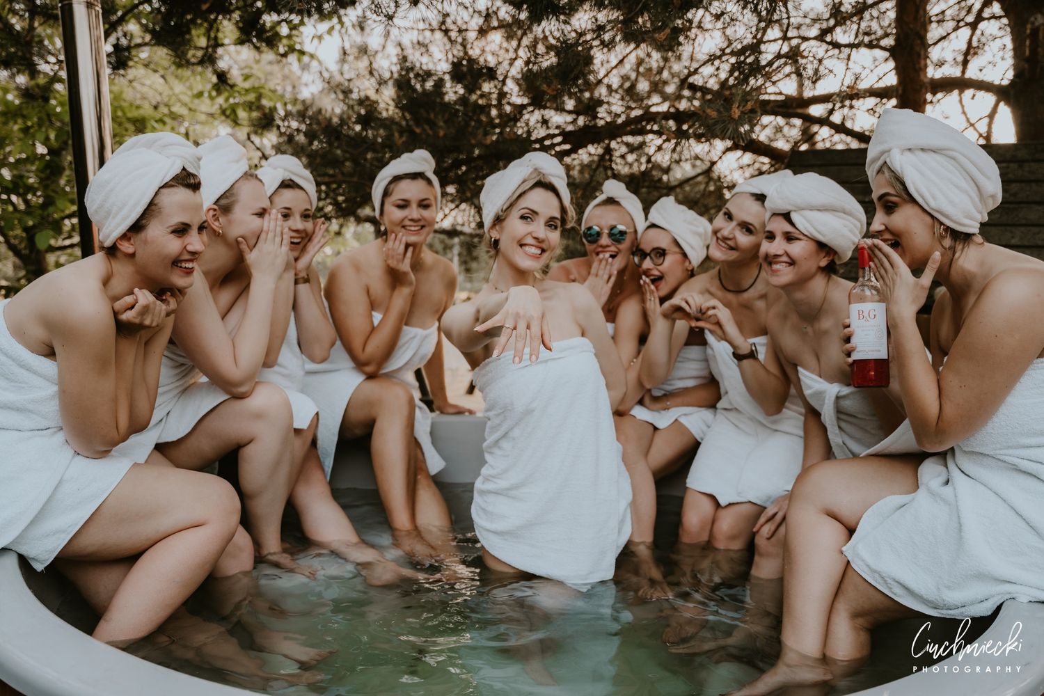 Group wearing white towels laughing together in a spa pool setting.